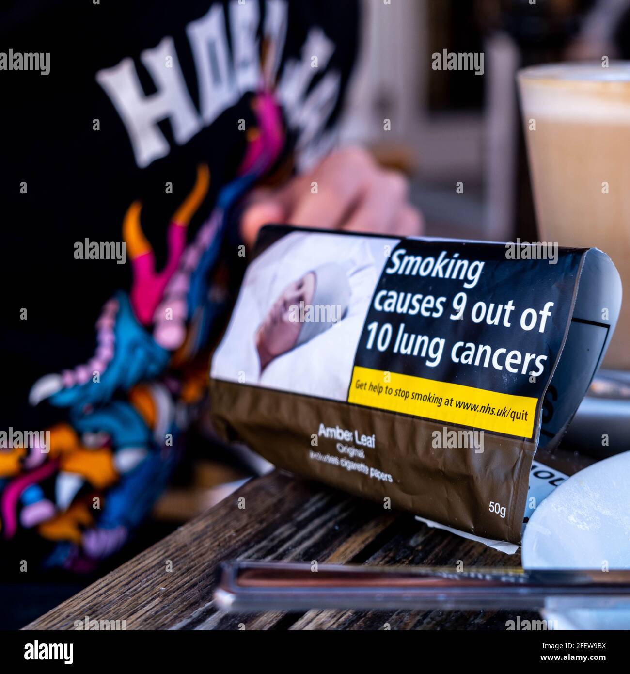 Epsom Surrey, London England, Großbritannien, April 23 2021, Packung mit rollendem Zigarettenrauch neben EINEM Latte Coffee auf EINER Tischplatte Stockfoto