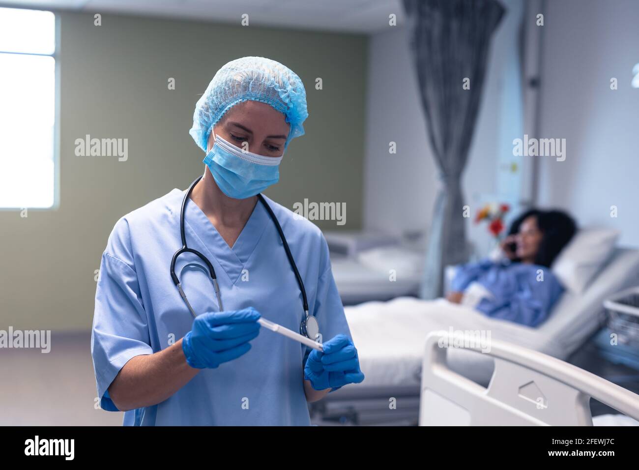 Kaukasische Ärztin im Krankenhaus trägt Gesichtsmaske und chirurgische Handschuhe, die den Abstrichtest halten Stockfoto