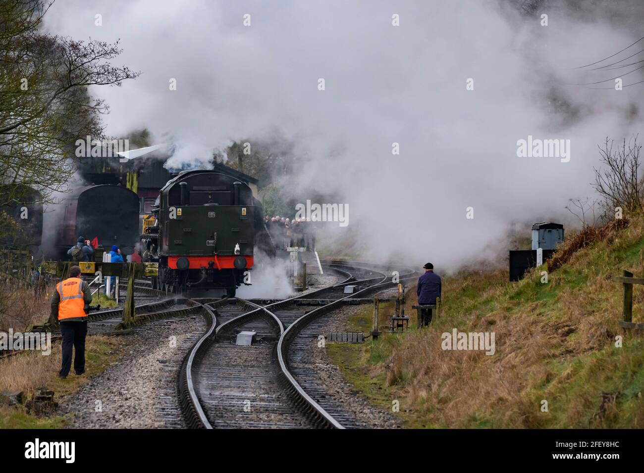 Historische Dampfeisenbahn oder Lok, die Rauchwolken aufblähen (Eisenbahner an den Punkten, Enthusiasten beobachten) - Oxenhope Station Sidings, Yorkshire England Großbritannien Stockfoto
