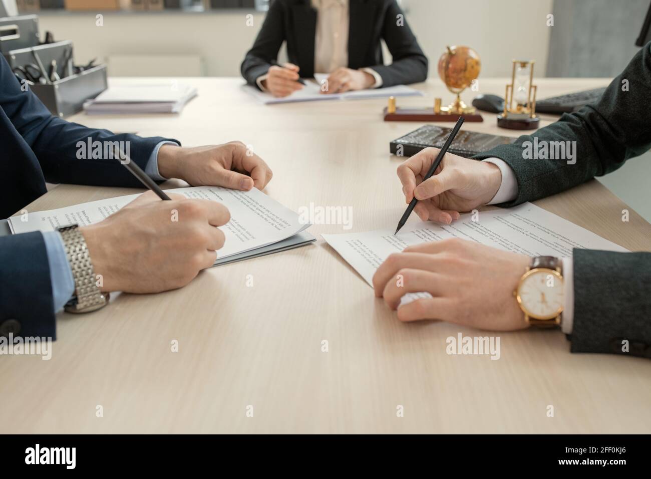 Nahaufnahme von nicht erkennbaren Anwälten in einer Armbanduhr, die sich gegenüber von beiden befindet Andere am Tisch und lesen Vertrag vor der Unterzeichnung bei der Sitzung Stockfoto