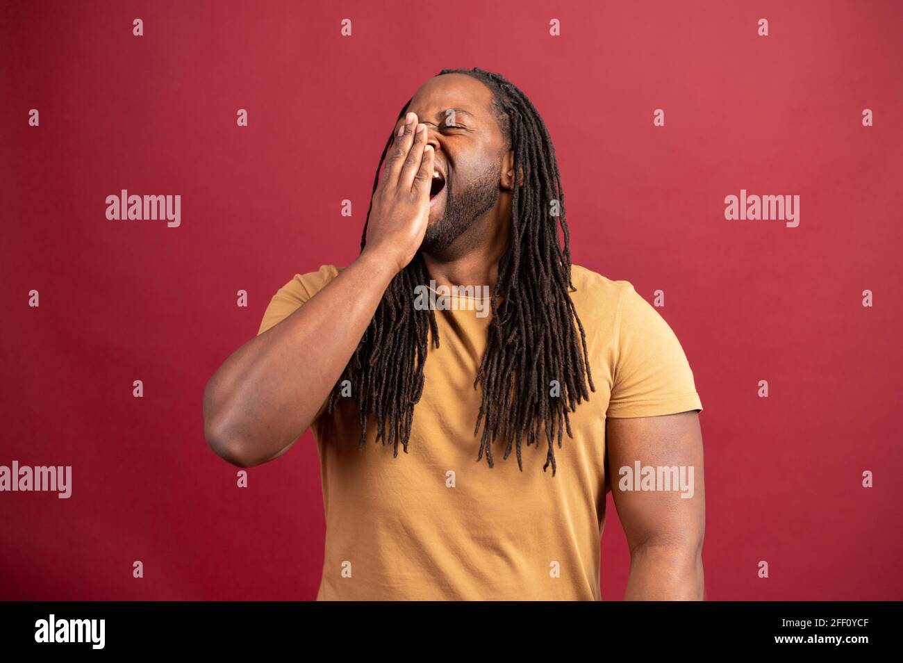 Schläfriger afroamerikanischer Kerl gähnt und fühlt sich auf rotem Hintergrund gelangweilt, müder schwarzer Mann fühlt Mangel an Energie und Schlaf, müde Mann muss sich ausruhen Stockfoto