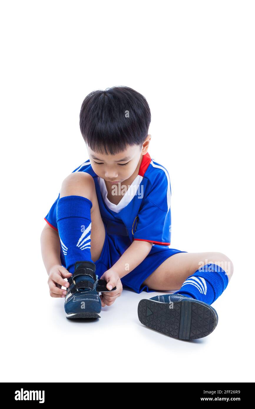 Junger asiatischer (thailändischer) Fußballspieler in blauer Uniform bindet Schuhe vor dem Fußballspielen. Kind bereitet sich auf den Wettkampf vor. Sportlicher Lifestyle. Isoliertes o Stockfoto