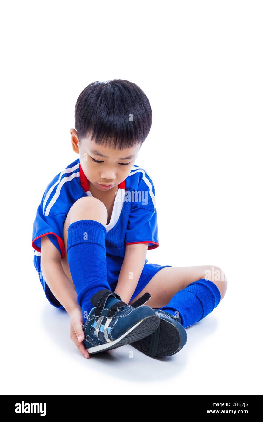 Jugend asiatische Fußballspieler in blauer Uniform binden Schuh vor dem Fußballspielen mit Schlagschatten.Kind Vorbereitung für den Wettbewerb. Sportlicher Lifestyle. Ist Stockfoto