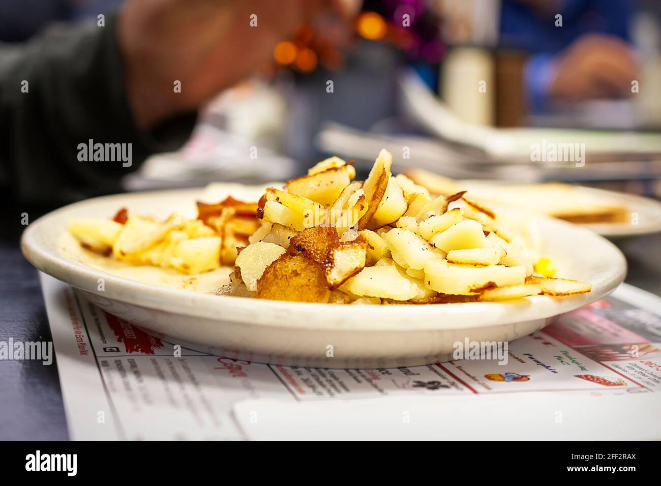 Ein Patron arbeitet an seinem Frühstücksteller, einschließlich einer großen Portion amerikanischer Kartoffeln oder Frühstückskartoffeln. Rest der Mahlzeit verschwommen im Hintergrund. Stockfoto