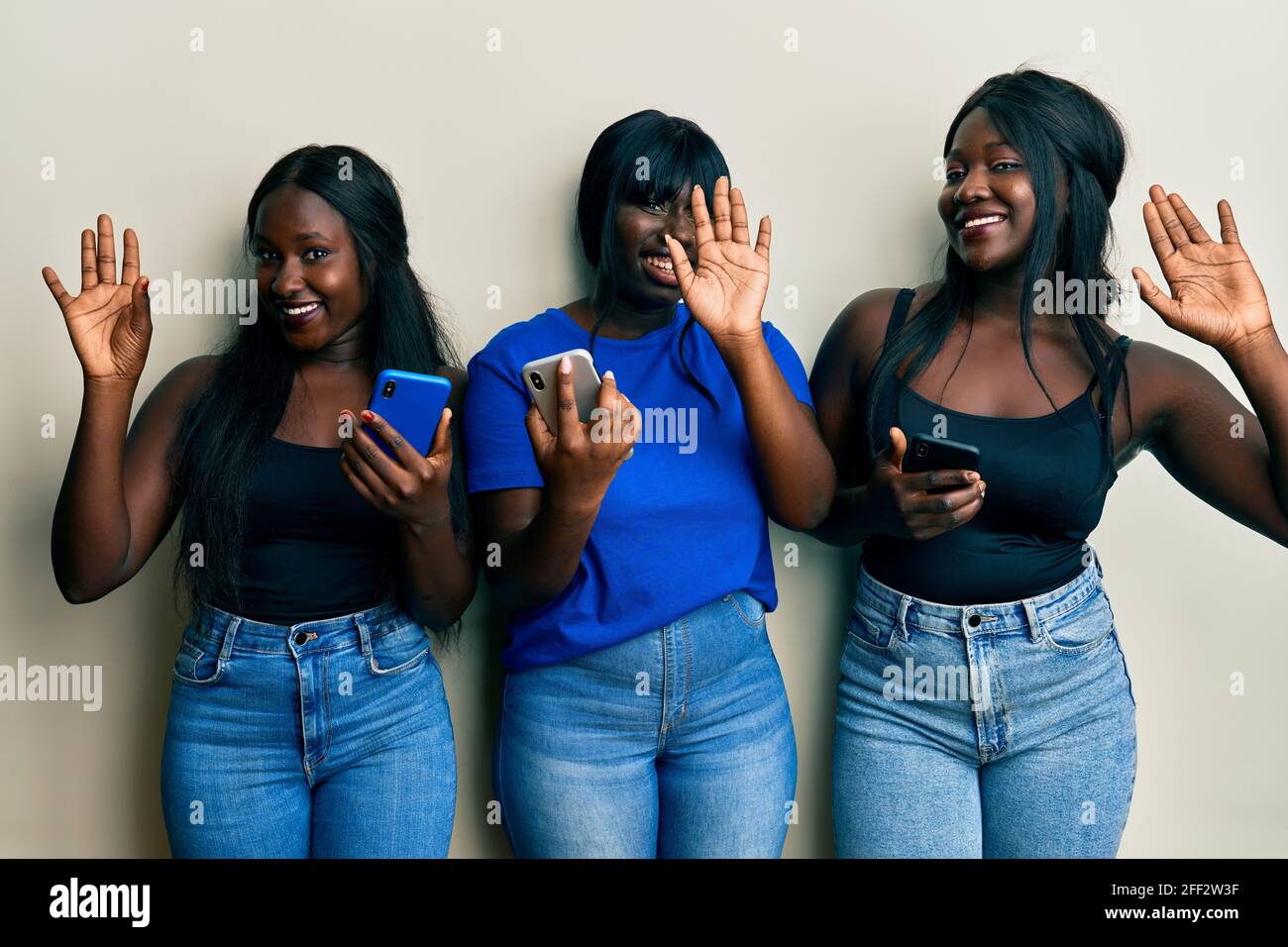 Drei junge afroamerikanische Freunde, die ihr Smartphone benutzen, sagen glücklich und lächelnd Hallo und freundlich Stockfoto