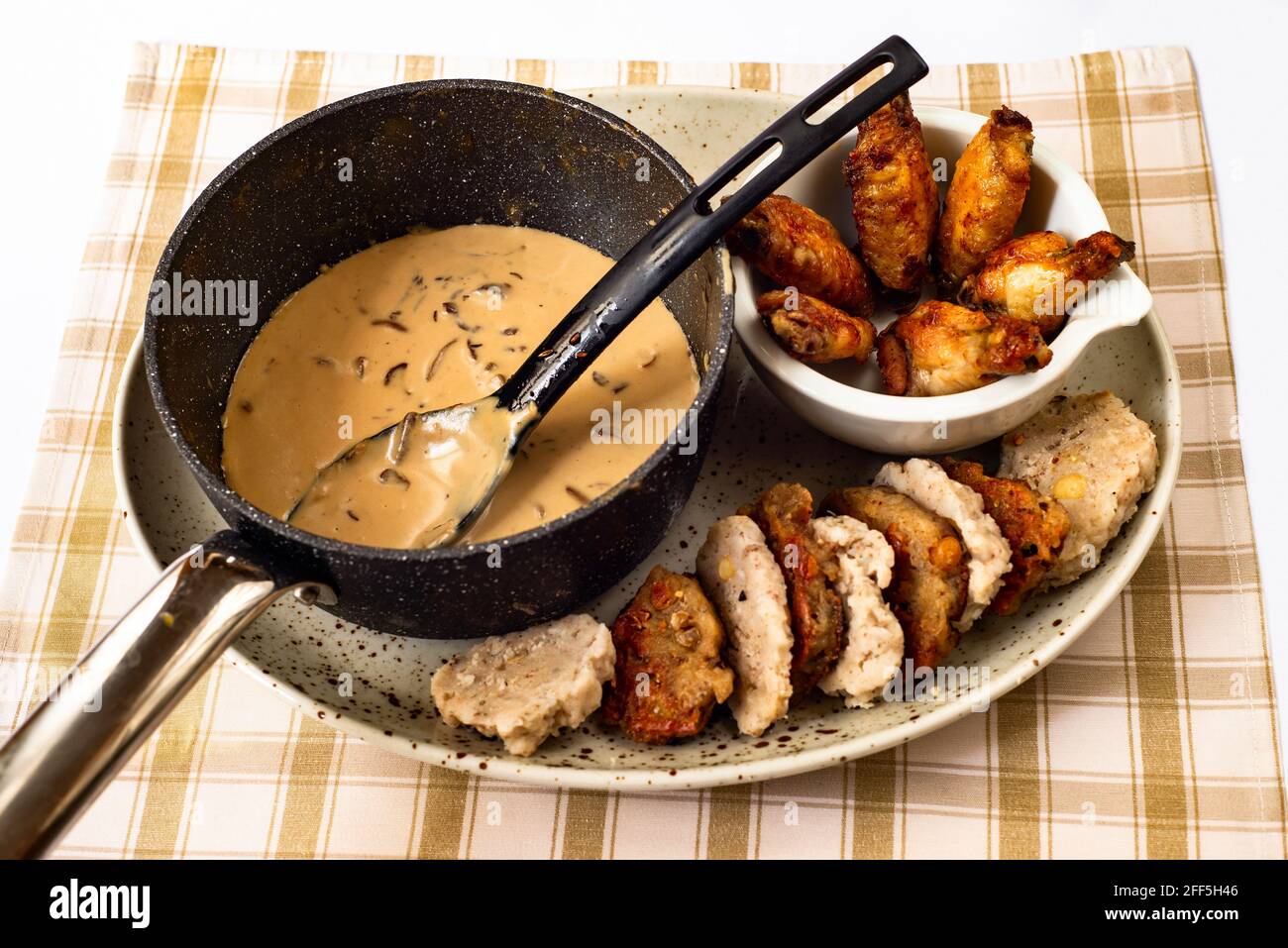 Pilzsauce im Topf mit Löffel, gegrillte Hähnchenschenkel in kleiner Schüssel, Knödel (abwechselnd in einer Reihe gekocht und gebraten) auf dem Teller auf dem Tisch. Stockfoto
