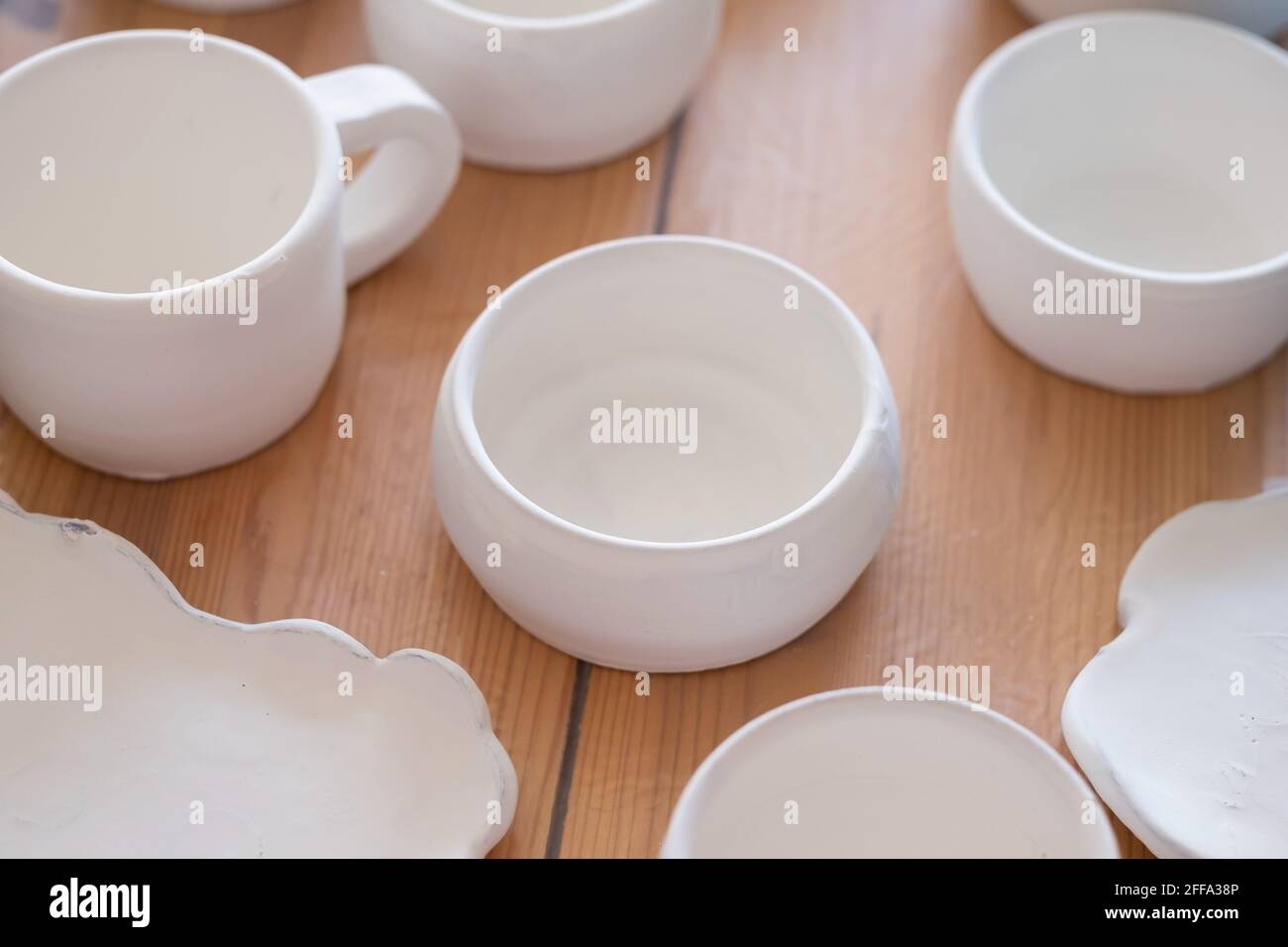 Handwerkliche Herstellung von weißen Tonbechern. Handgemachte Keramik vor dem Brennen stehend auf dem Tisch Stockfoto