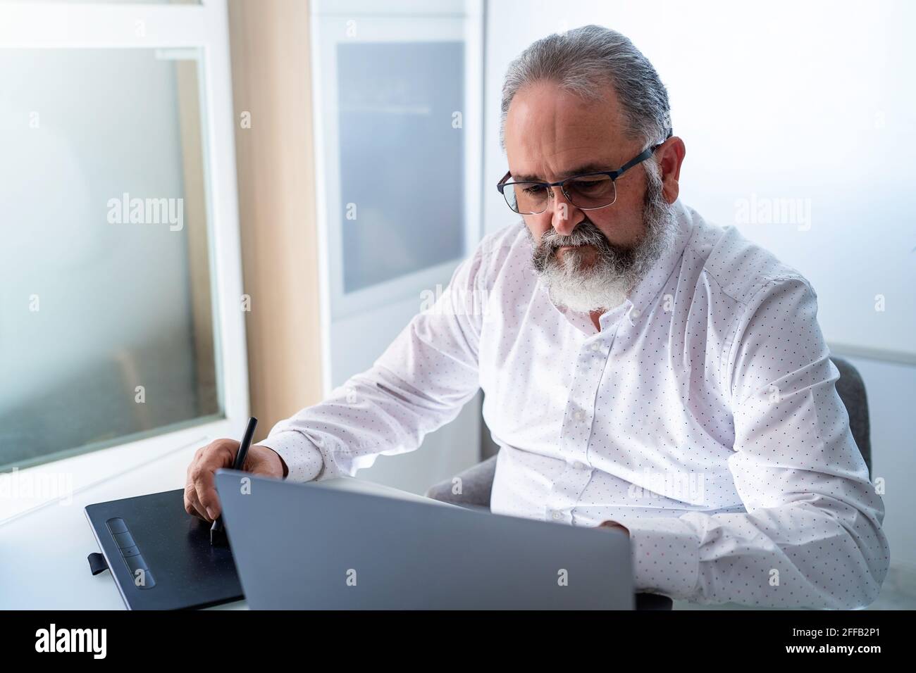 Älterer Mann, der zu Hause mit Laptop und Tablet arbeitet Stockfoto