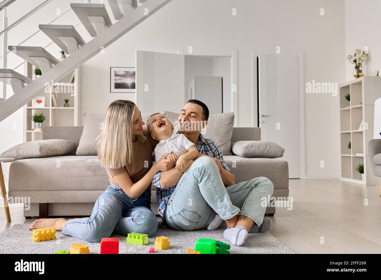Glückliche junge Erwachsene Eltern mit Kind sitzen auf dem Boden im modernen Wohnzimmer. Stockfoto