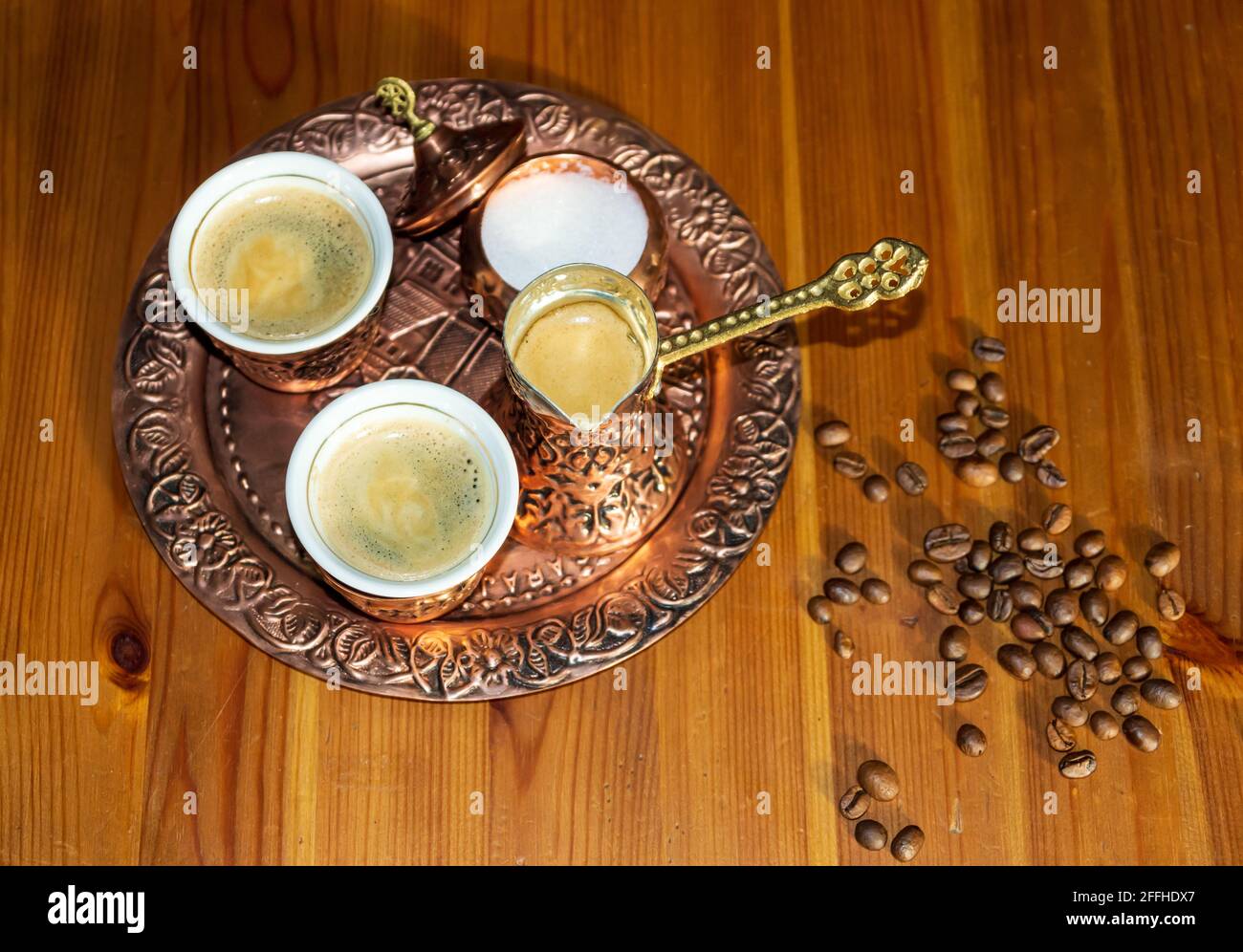 Türkischer Kaffee in Kupferbecher und -Topf serviert.Kaffeebohnen auf braunem Holztisch. Stockfoto