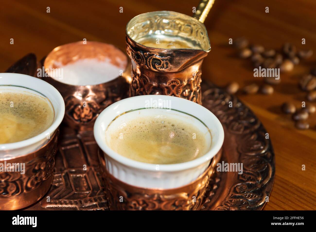 Türkischer Kaffee in Kupferbecher und -Topf serviert.Kaffeebohnen auf braunem Holztisch. Stockfoto