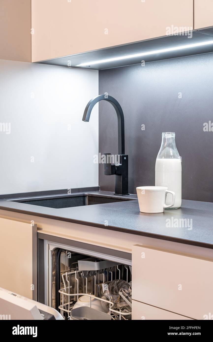 Moderner schwarzer Wasserhahn in einer minimalistischen Küche und einer Spülmaschine. Theke aus dunklem Stein mit Waschbecken. Stockfoto