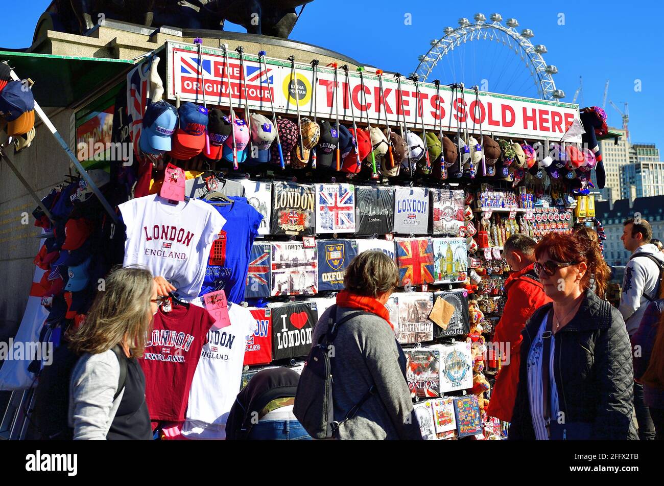 London, England, Vereinigtes Königreich. Touristen an und um einen Souvenirstand in der Nähe der Houses of Parliament an einem sonnigen Morgen in London. Stockfoto