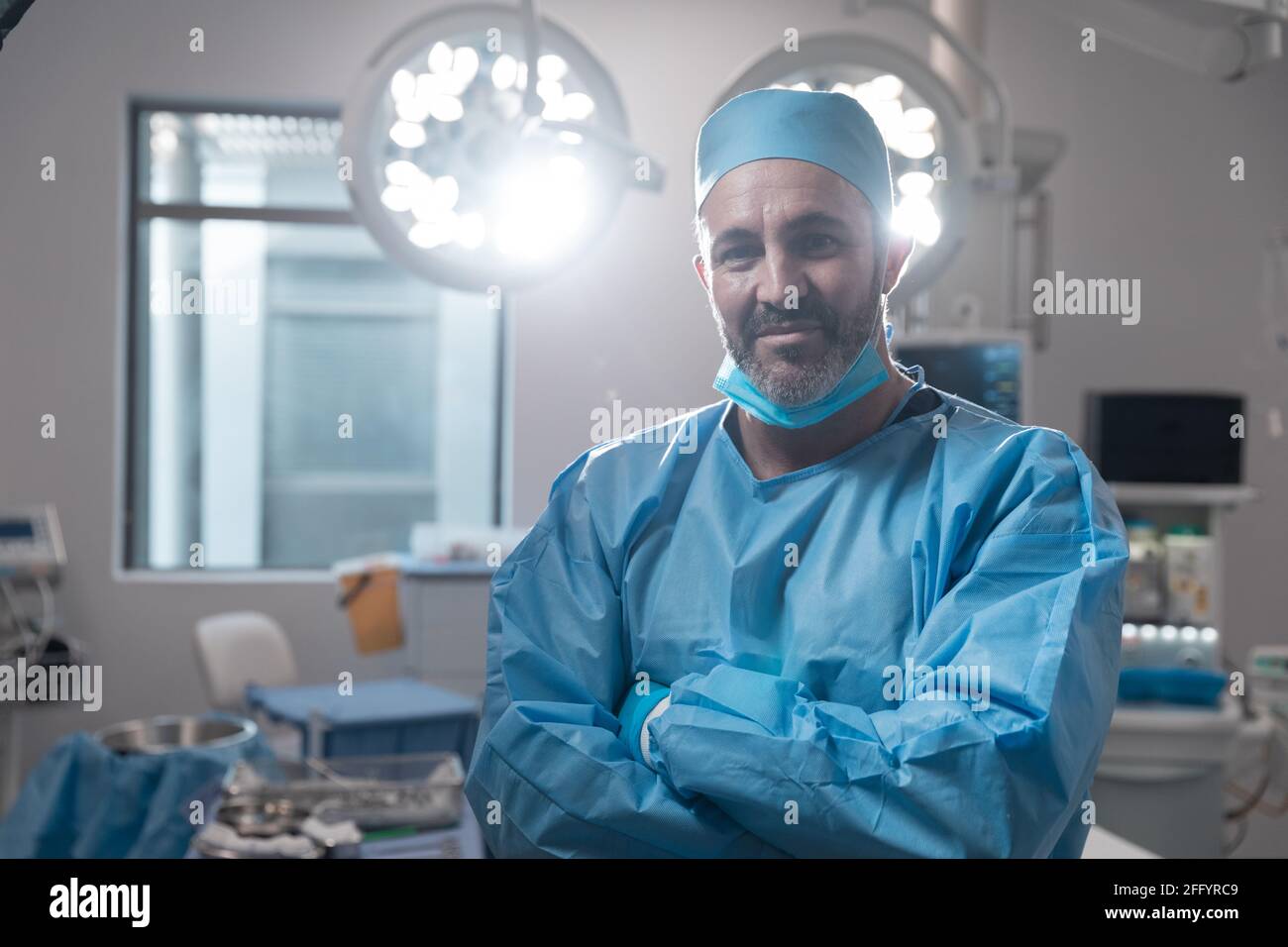 Lächelnder kaukasischer Chirurg mit Gesichtsmaske und Schutzkleidung Im Operationssaal Stockfoto