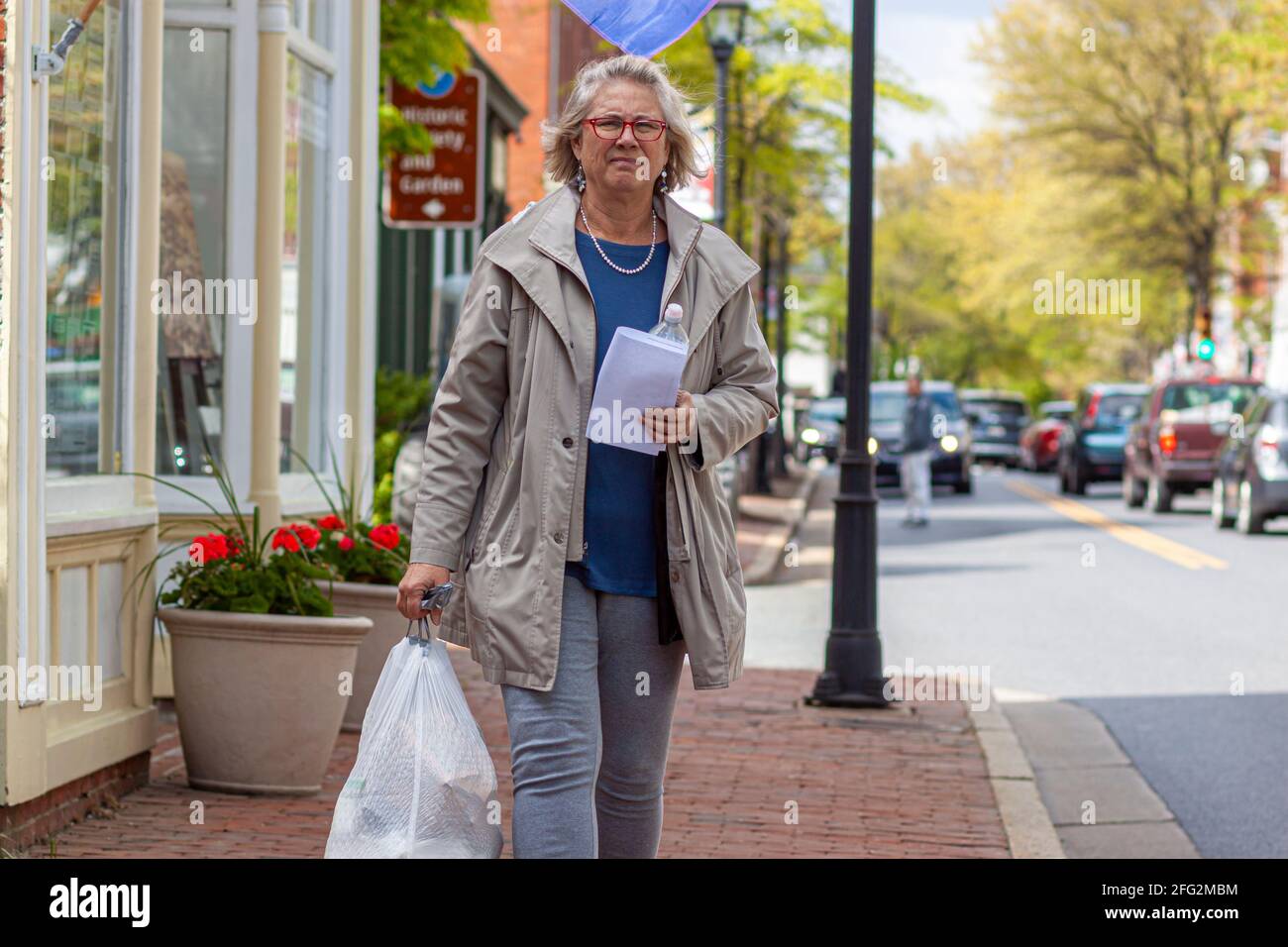 Easton, MD, USA 04-16-2021: Eine blonde ältere Frau trägt einen vollen Beutel mit Müll in schweren weißen Mülltüten mit gequetschter Oberseite und Griff. Müll Stockfoto