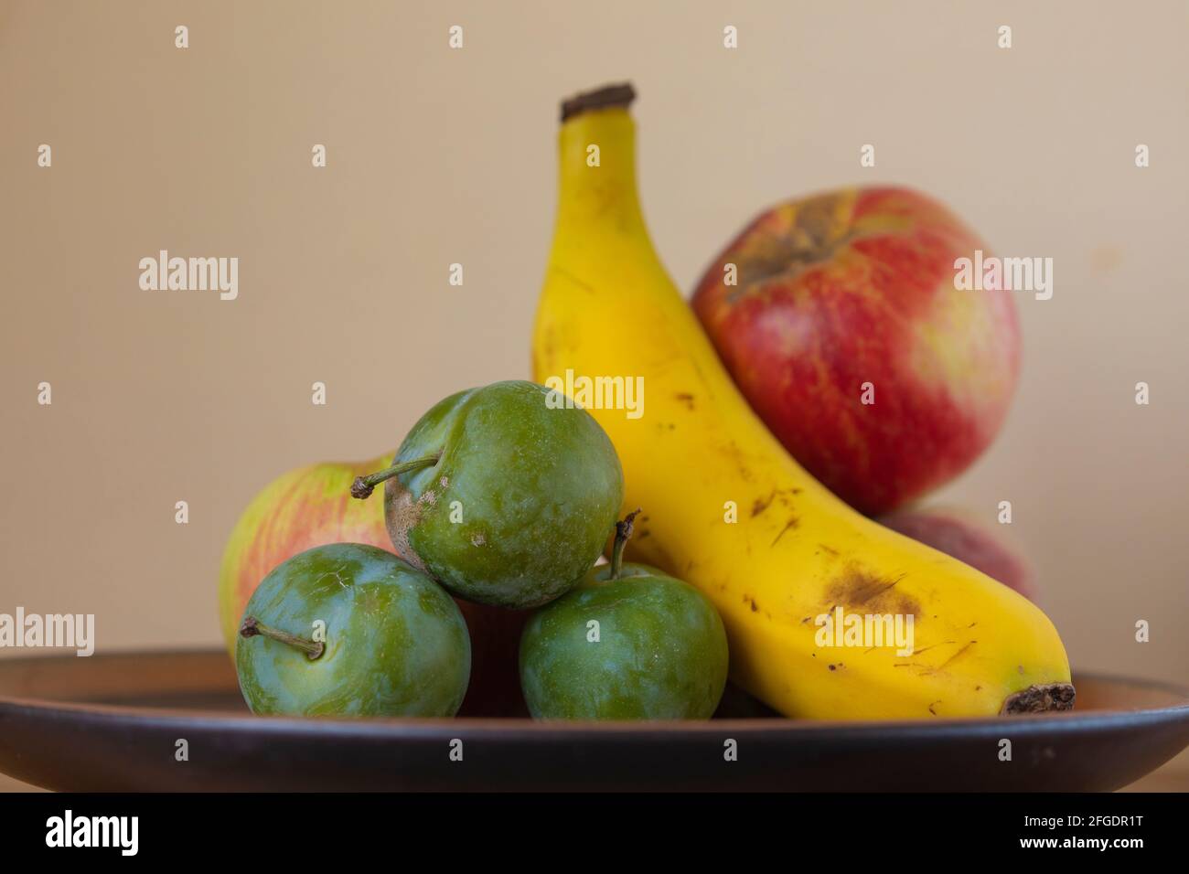 Hausgemachte Stillleben von einem Teller mit saisonalen Früchten, ein köstliches vegetarisches Dessert aus Bananen, Apfel und Pflaumen. Rohe, gesunde und unverarbeitete Lebensmittel, lecker Stockfoto