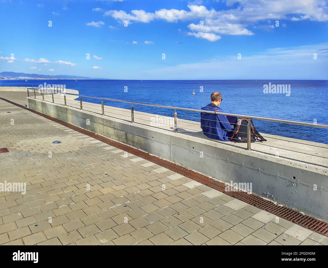 Rückansicht eines älteren Mannes, der auf einer Promenade in der Nähe des Meeres sitzt. Stockfoto