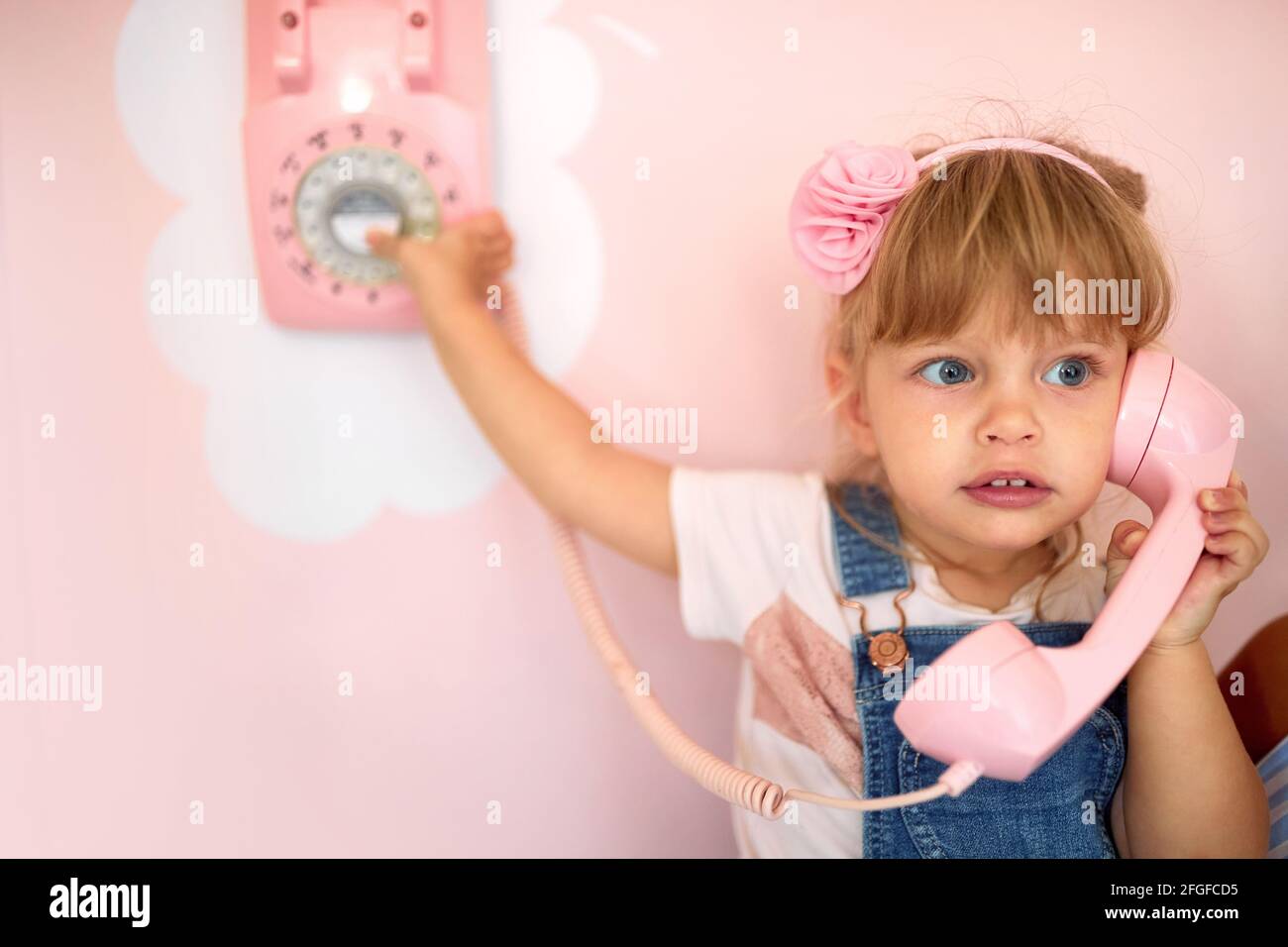 Ein kleines Mädchen spielt mit einem Retro-Telefon an der Wand einer Konditorei in einer angenehmen Atmosphäre. Konditorei, Dessert, süß Stockfoto