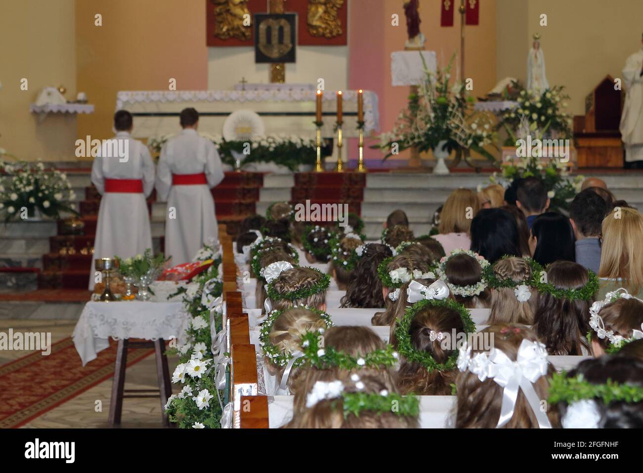 Kinder im Inneren während der Feier erste heilige Kommunion Zeremonie, Mädchen in weißen Kleidern, Kranz, Altar, Priester. Stockfoto