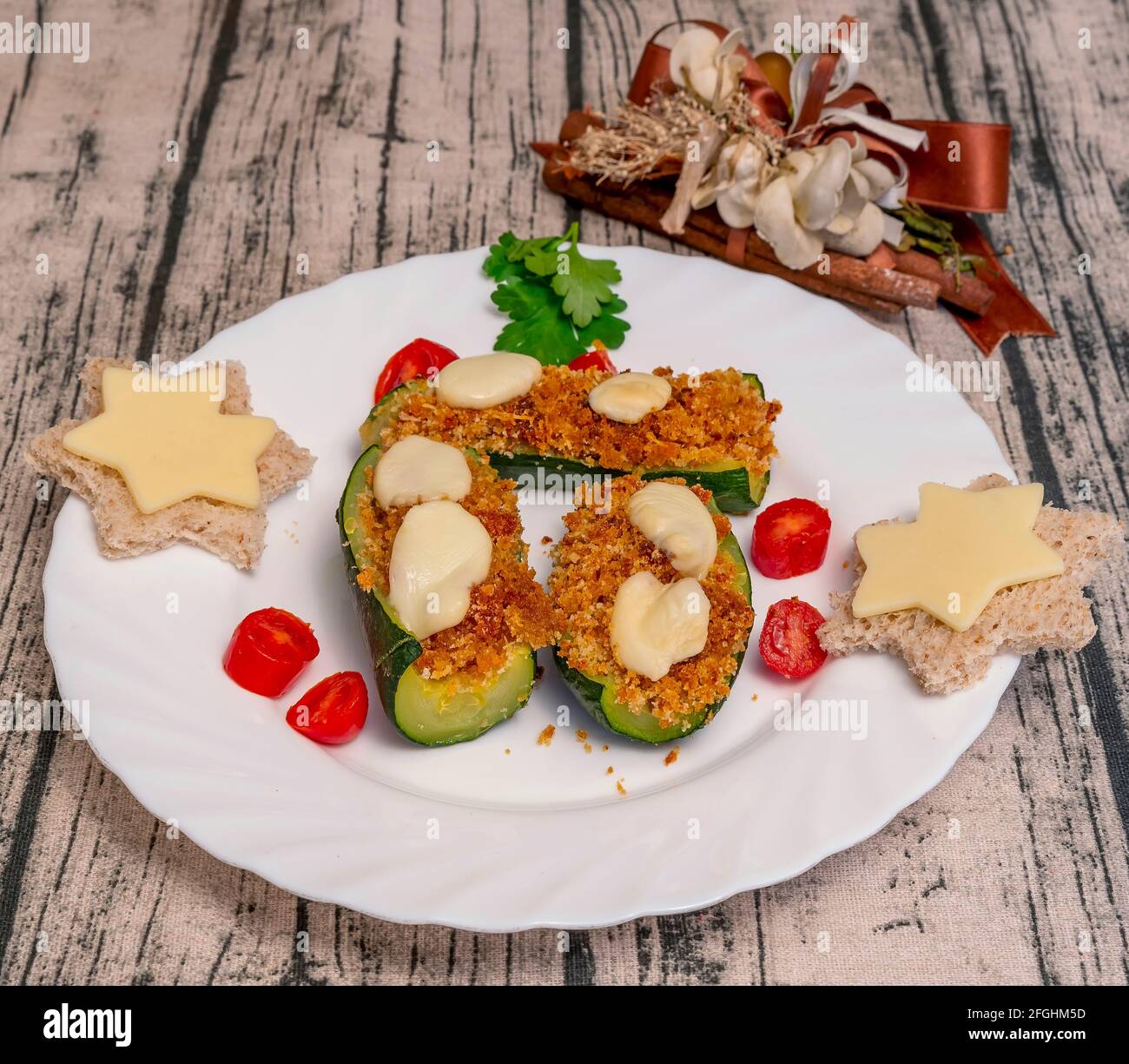 Zucchini gefüllt mit Paniermehl, Tomaten und emmentaler Käse, mit sternförmigem Brot und Petersilienblättern Stockfoto