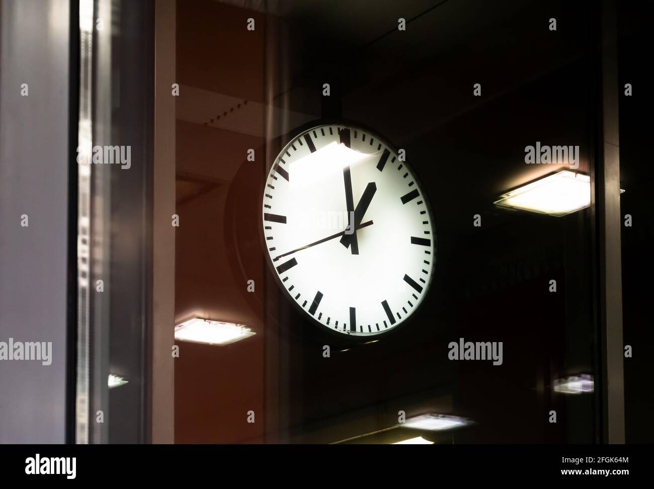 Eine einzelne Uhr mit Hintergrundbeleuchtung auf einem abgedunkelten Bahnhofsplatz, Nahaufnahme von Objekten im öffentlichen Bereich. Pendeln Transport Rush Hour, Eile und Eile, p Stockfoto
