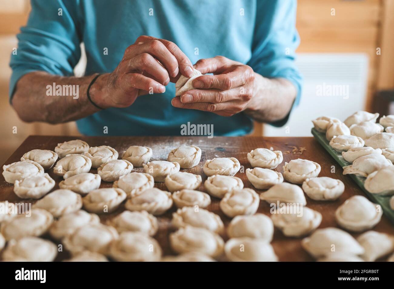 Hände von Senior Mann Kochen und Formen kleine hausgemachte ungekochte Knödel mit Fleisch auf Küchentisch. Nationale traditionelle russische Küche. Tun Sie es Ihre Stockfoto