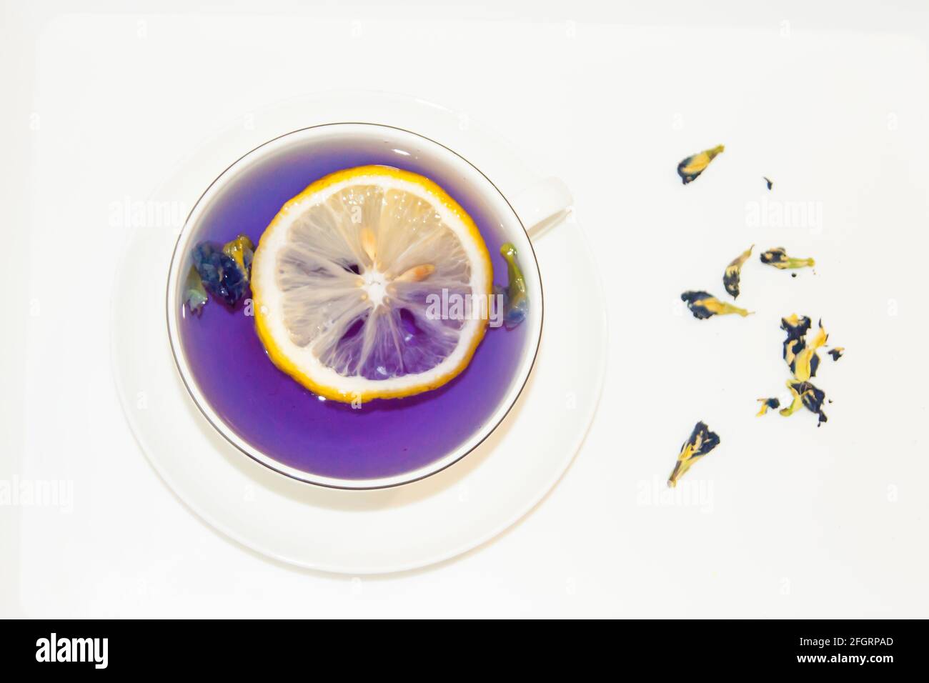 Die Stimmungsfarbe ist blau - blauer Tee mit Zitrone in einem weißen Becher, der auf einer weißen Untertasse und weißem Tablett steht. Kontrast. Nützliche Getränke, heilende Eigenschaft Stockfoto
