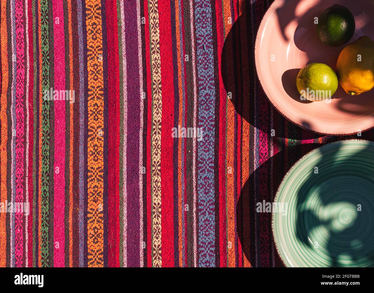 Bild von rosa und pastellgrünen Suppentellern, zwei Zitronen und Kalk auf einem farbenfrohen Tischtuch, das im Sonnenlicht aufgenommen wurde Stockfoto