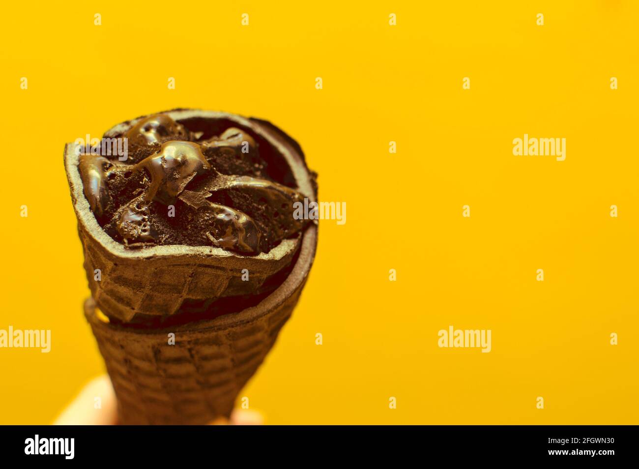 Schwarzes Eis in einem Waffelkegel auf gelbem Hintergrund. Stockfoto