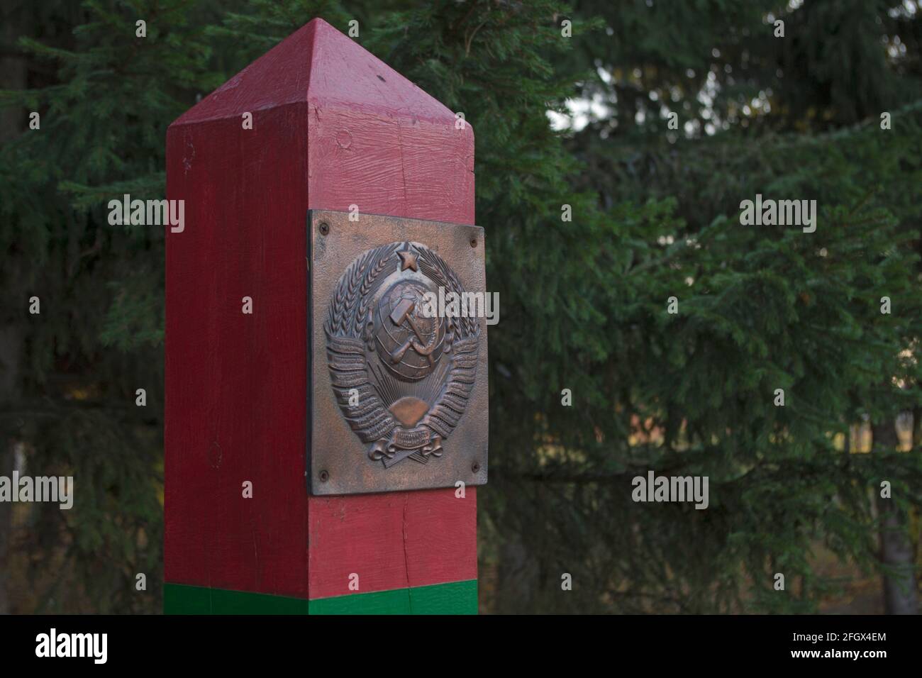 Die Oberseite des hölzernen Grenzpfosten in Grün und gemalt Rote horizontale Streifen mit einer Metallplatte, die das Fell darstellt Der Waffen der UdSSR, die in ihr befestigt sind Stockfoto