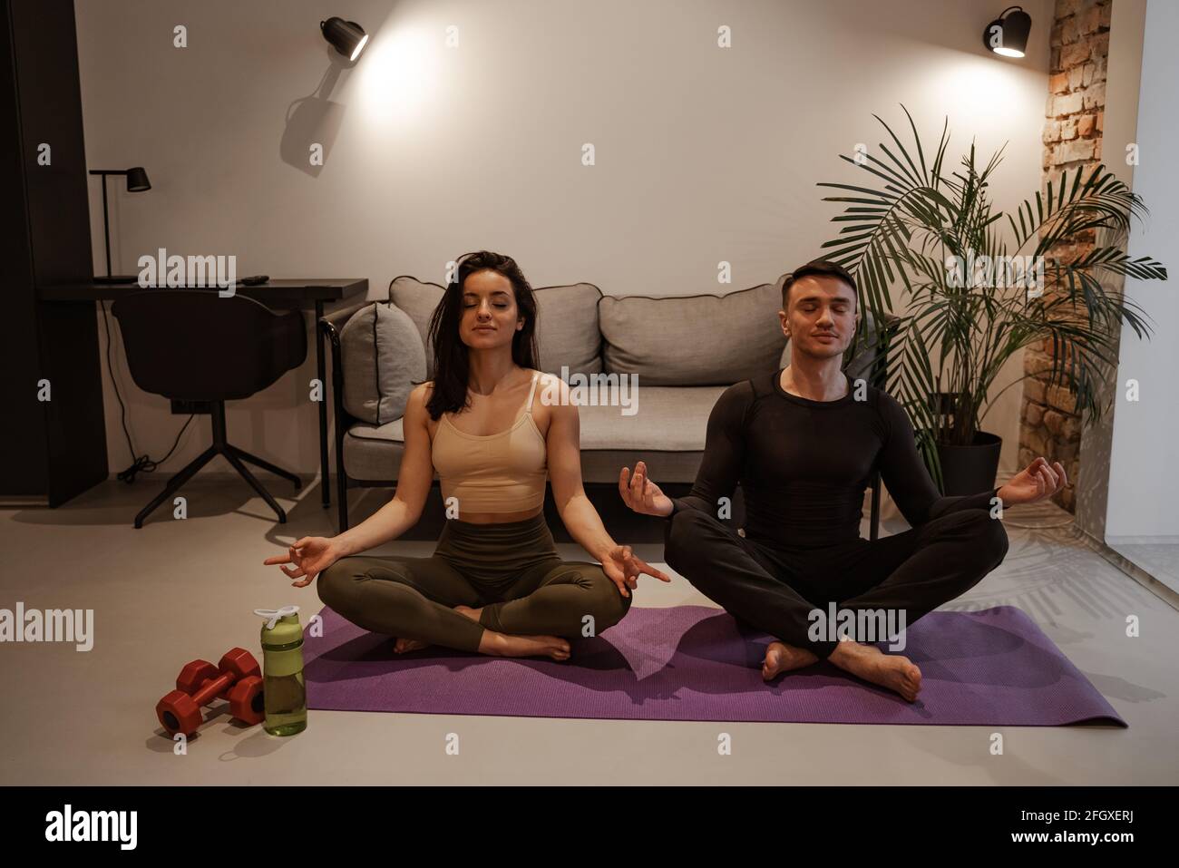 Yoga für zwei zu Hause Konzept. Junge Muschina und eine Frau sitzen in Asanas auf einer Yogamatte in einer Wohnung und meditieren. Stockfoto