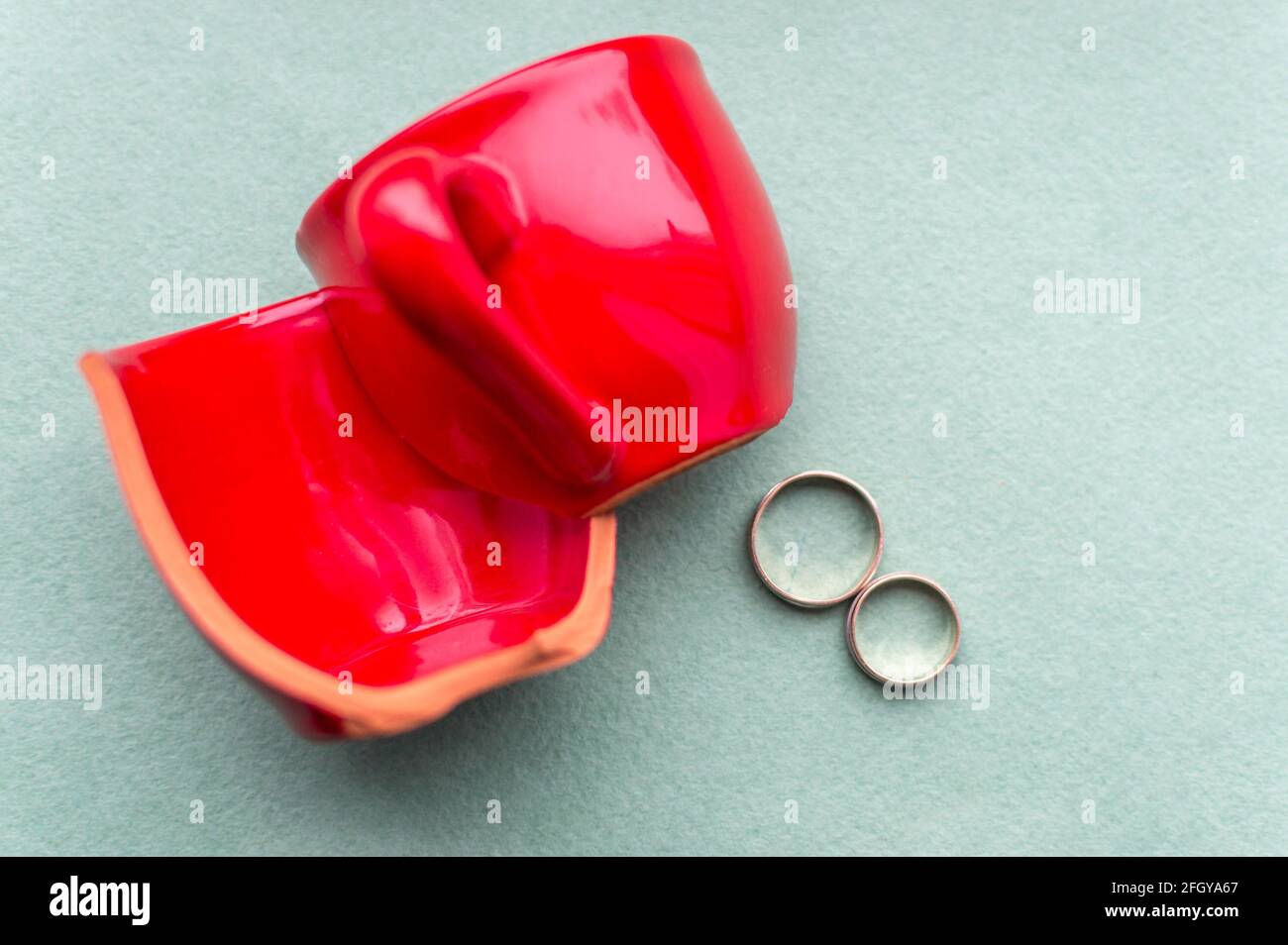 Zerbrochene rote Tasse und Eheringe. Konzept Scheidung Stockfoto