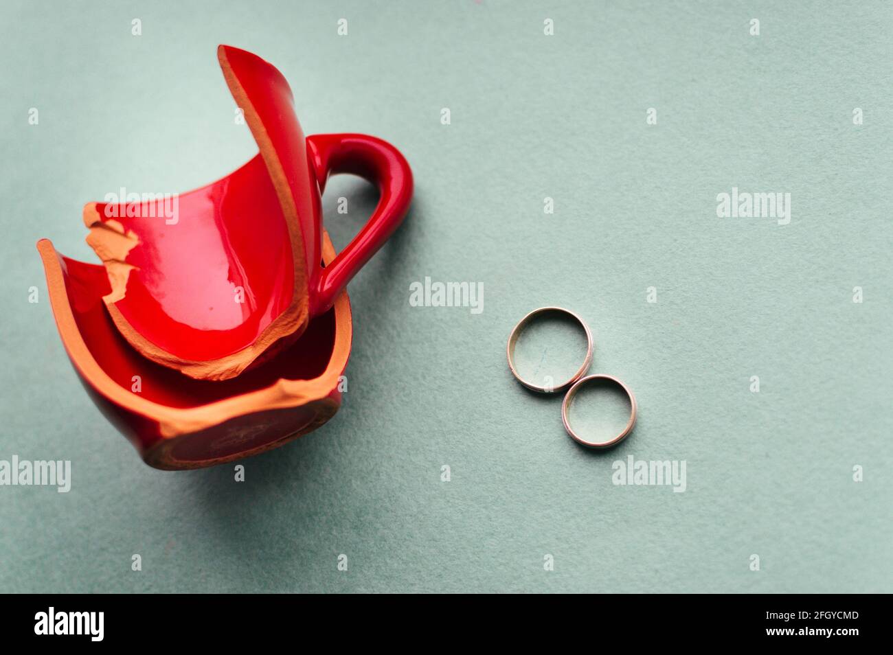 Zerbrochene rote Tasse und Eheringe. Konzepttrennung Stockfoto