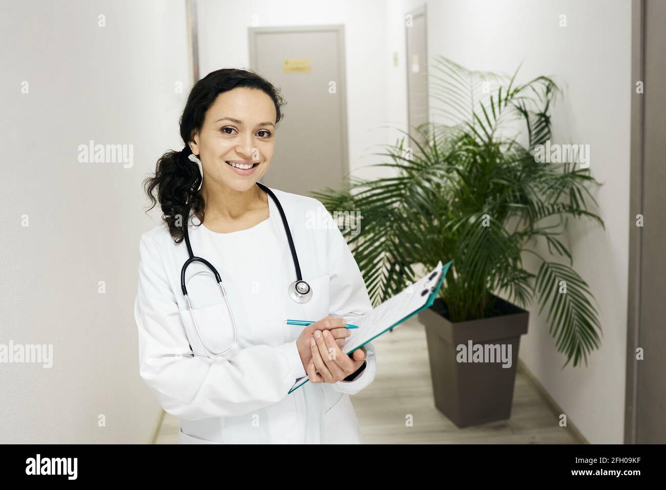 Arztberuf. Brünette Hausärztin mit Patientenakte in der Hand stehend in einer Klinik, Porträt Stockfoto