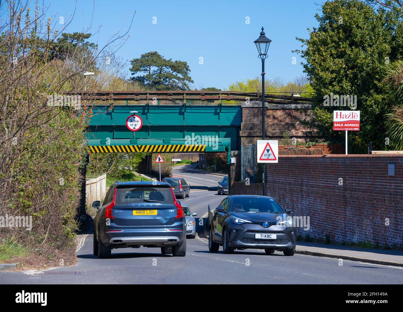 Autos und andere Fahrzeuge, die auf einer britischen Straße unter einer niedrigen Eisenbahnbrücke mit einem Höhenbegrenzungsschild in Emsworth, Hampshire, England, Großbritannien, fahren. Stockfoto