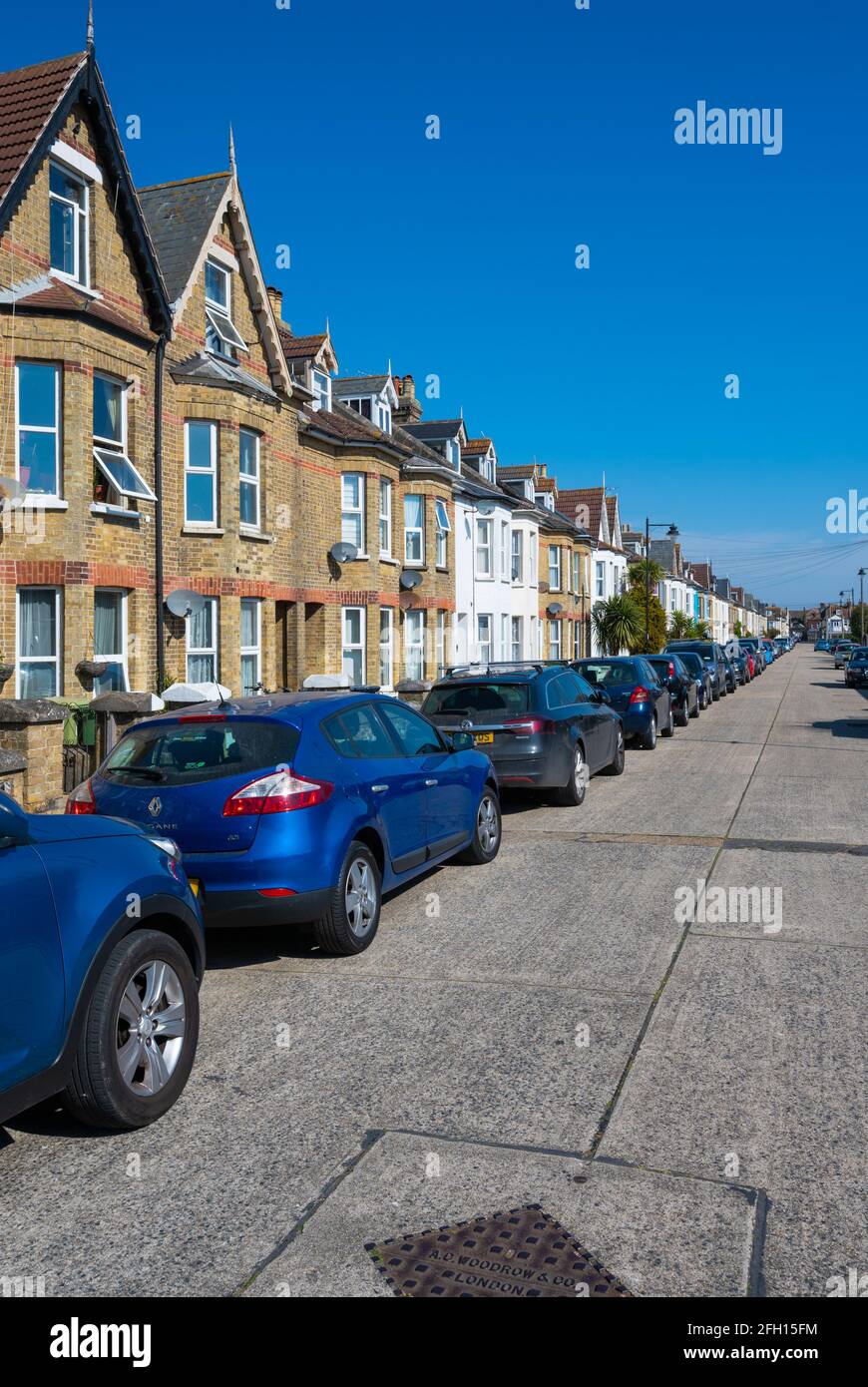 Wohnstraße von viktorianischen Reihenhäusern ohne Fahrten und Parken auf der Straße mit Autos, die entlang der Straßenlänge in West Sussex, England, Großbritannien, geparkt sind. Stockfoto