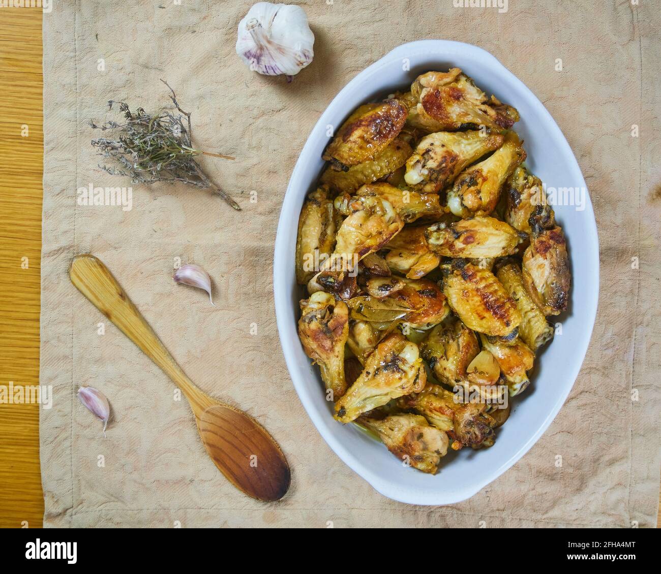 Knoblauch-Hühnerflügel (Pollo al ajillo). Spanisches Tapas-Gericht in einer Keramikplatte serviert mit serviert mit Knoblauchhandschuhen, Blumen und einem Holzlöffel. Oben Stockfoto