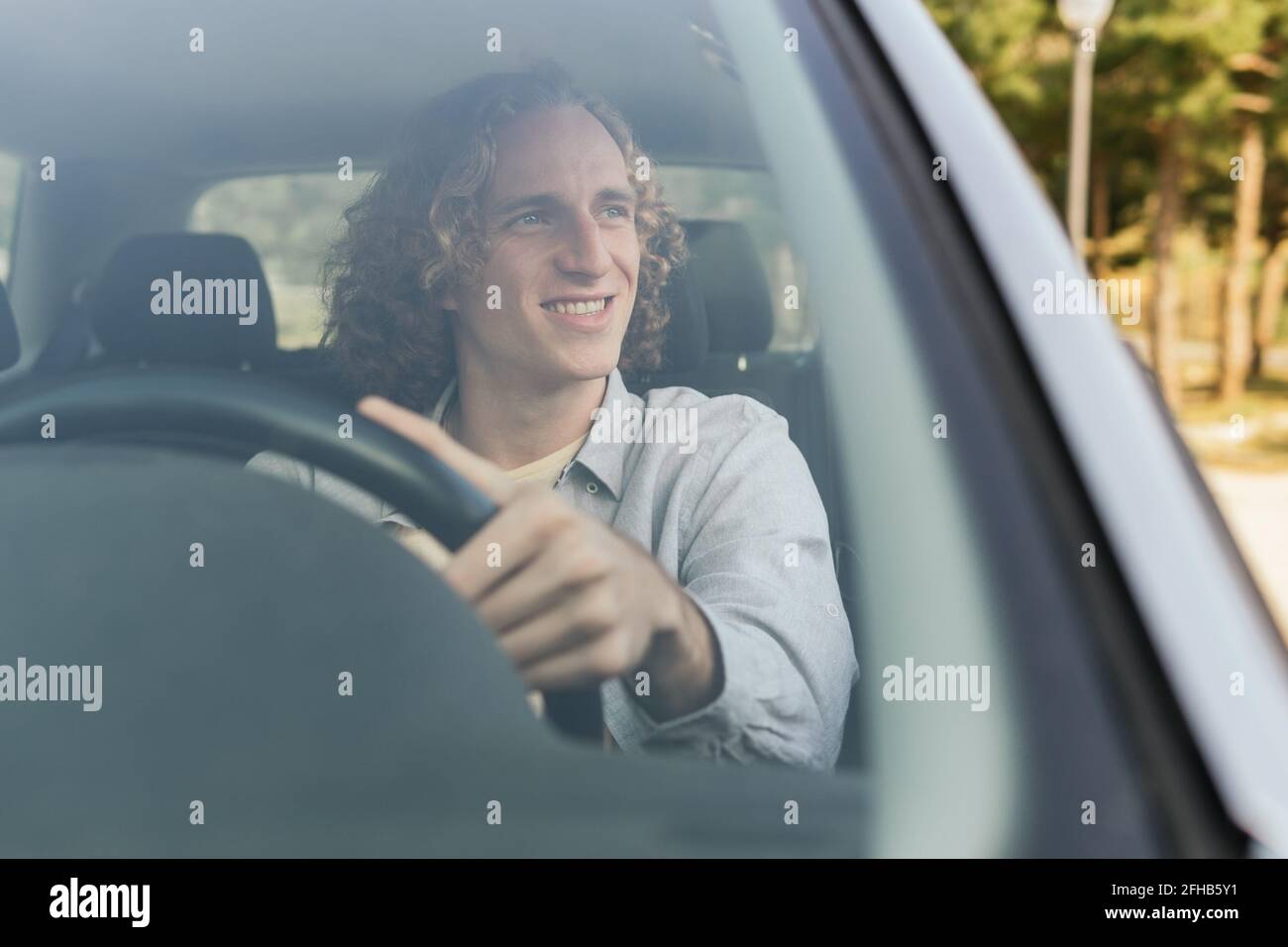 Glücklich junge behaarte Männchen schaut weg durch offenes Fenster von Auto, während Sie auf dem Fahrersitz sitzen Stockfoto