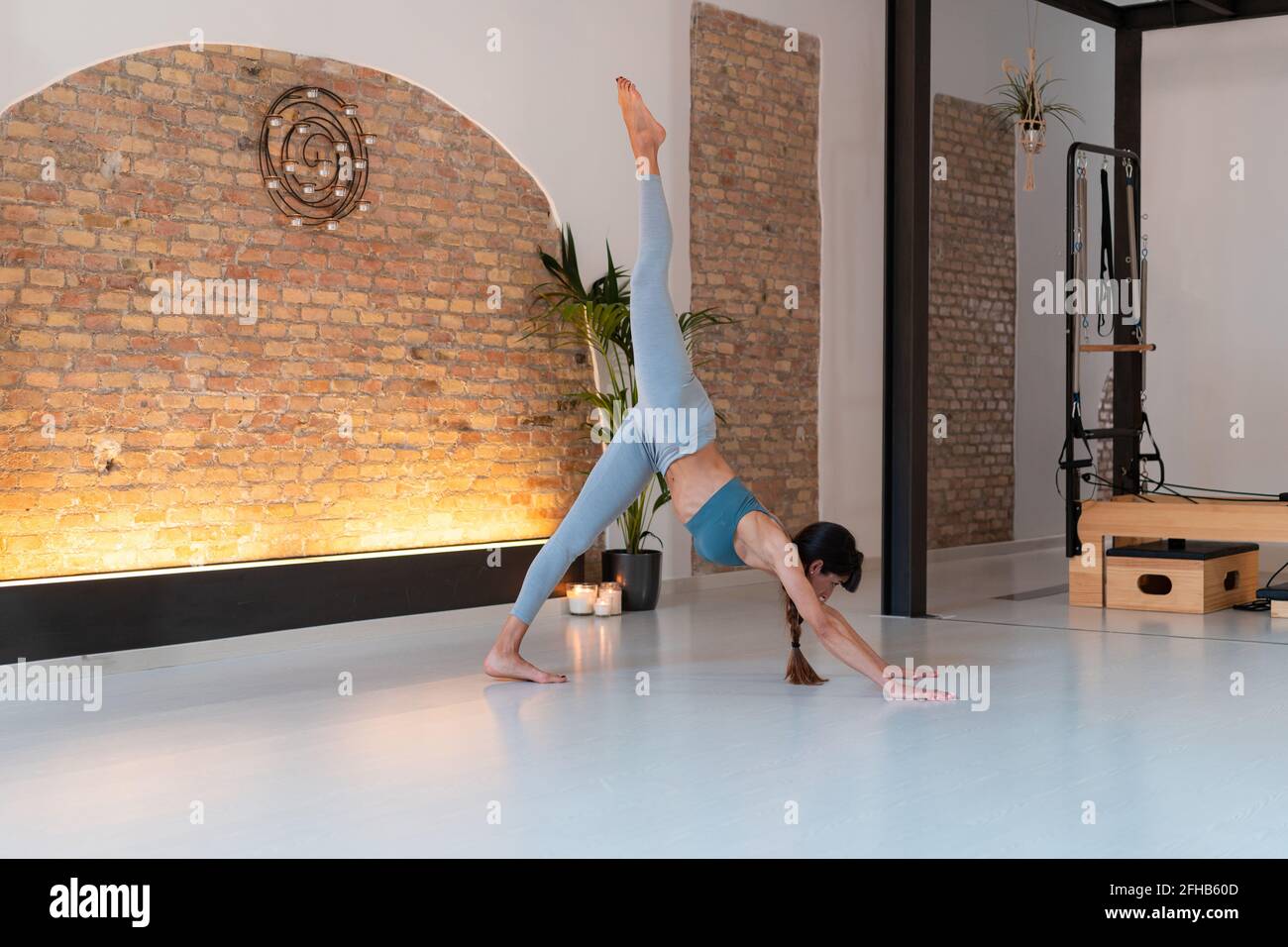 Seitenansicht einer schlanken Frau, die in Tri Pada Yoga praktiziert Adho Mukha Svanasana beim Strecken der Beine im Fitnessstudio Stockfoto