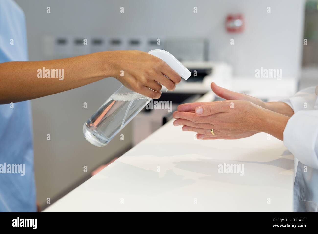 Mittelteil einer weiblichen Rezeptionistin, die die Hände einer Ärztin desinfiziert Über den Ladentisch im Krankenhaus Stockfoto