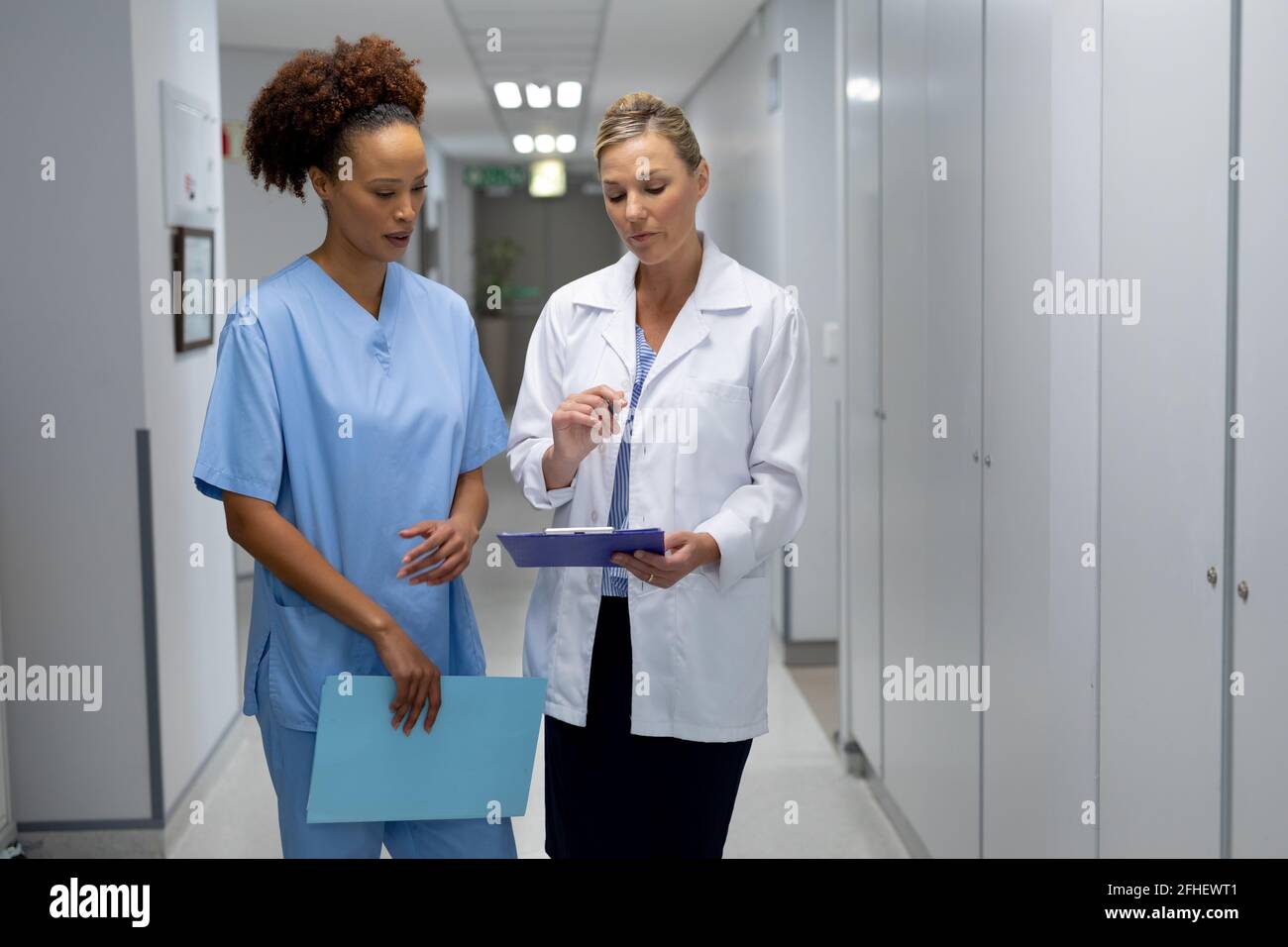 Zwei verschiedene Ärztinnen, die im Krankenhausflur stehen und sie betrachten Dokument mit medizinischen Diagrammen Stockfoto
