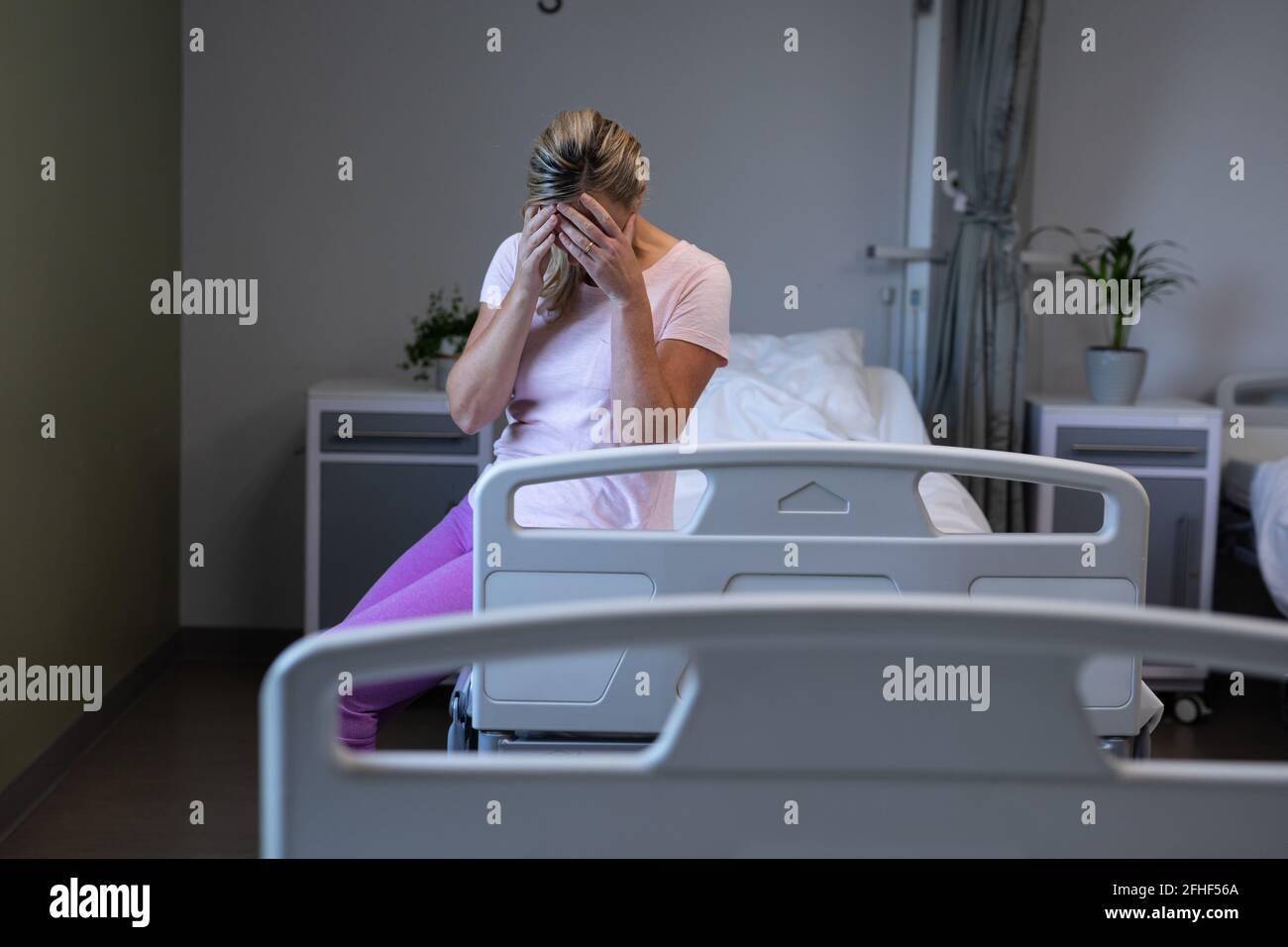 Kaukasische Patientin, die im Patientenzimmer auf dem Krankenhausbett sitzt Beunruhigend Stockfoto