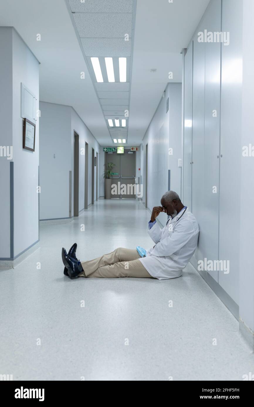 afroamerikanischer Arzt, der auf dem Boden im Krankenhausflur sitzt Und besorgniserregend Stockfoto