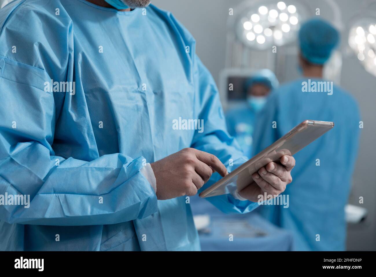 Mittelteil des kaukasischen männlichen Chirurgen, der Schutzkleidung mit einer Tablette trägt Im Operationssaal Stockfoto