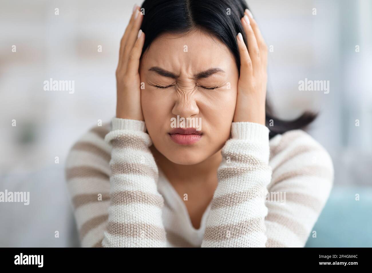 Emotionale Asiatische Frau, Die Zu Hause Die Ohren Mit Den Händen Bedeckt Stockfoto