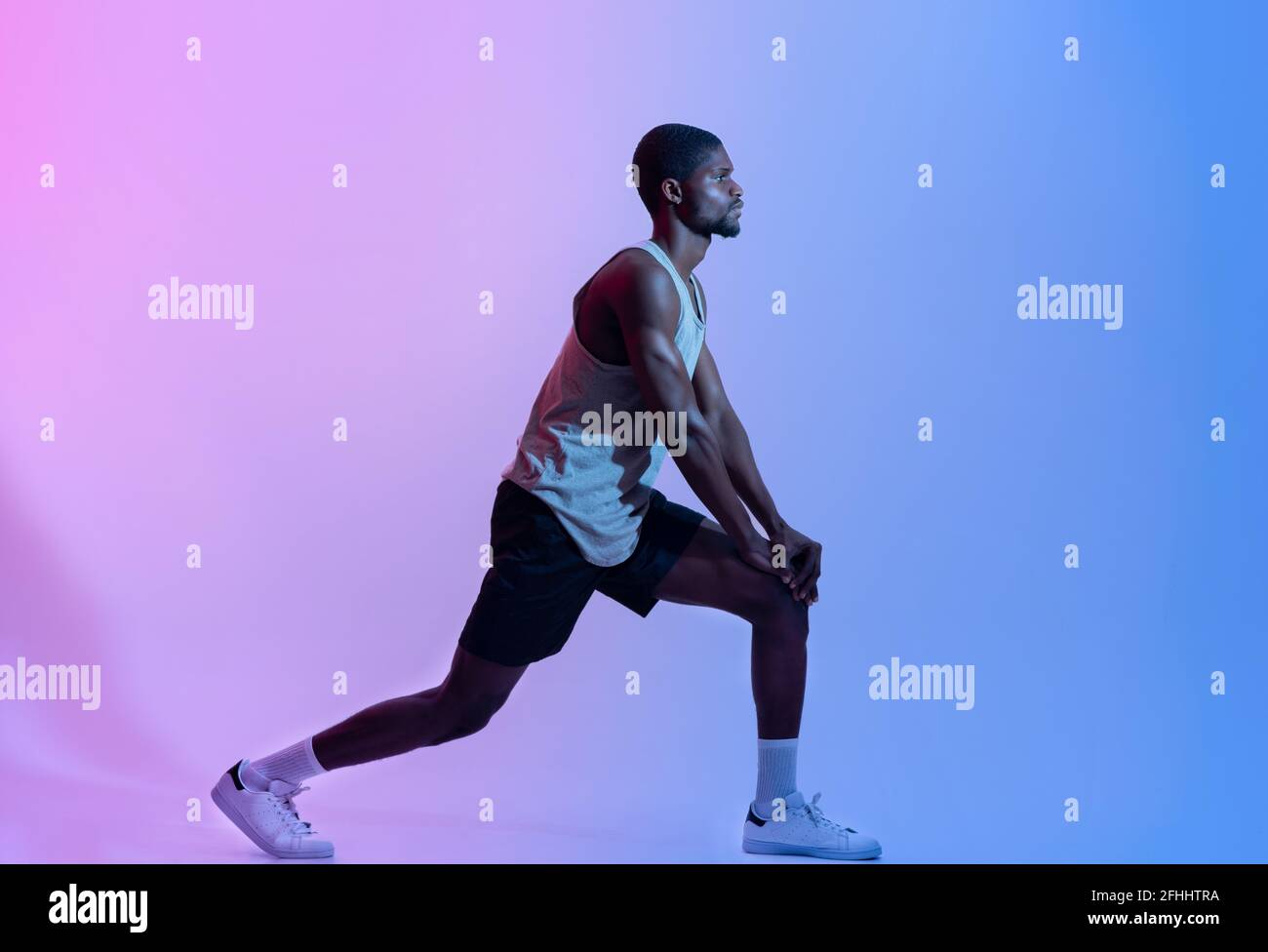 Seitenansicht des fitgen schwarzen Mannes in Sportswear, der Ausfallschritte im neonfarbenen, langen Porträt macht. Gesundes Wohnkonzept Stockfoto