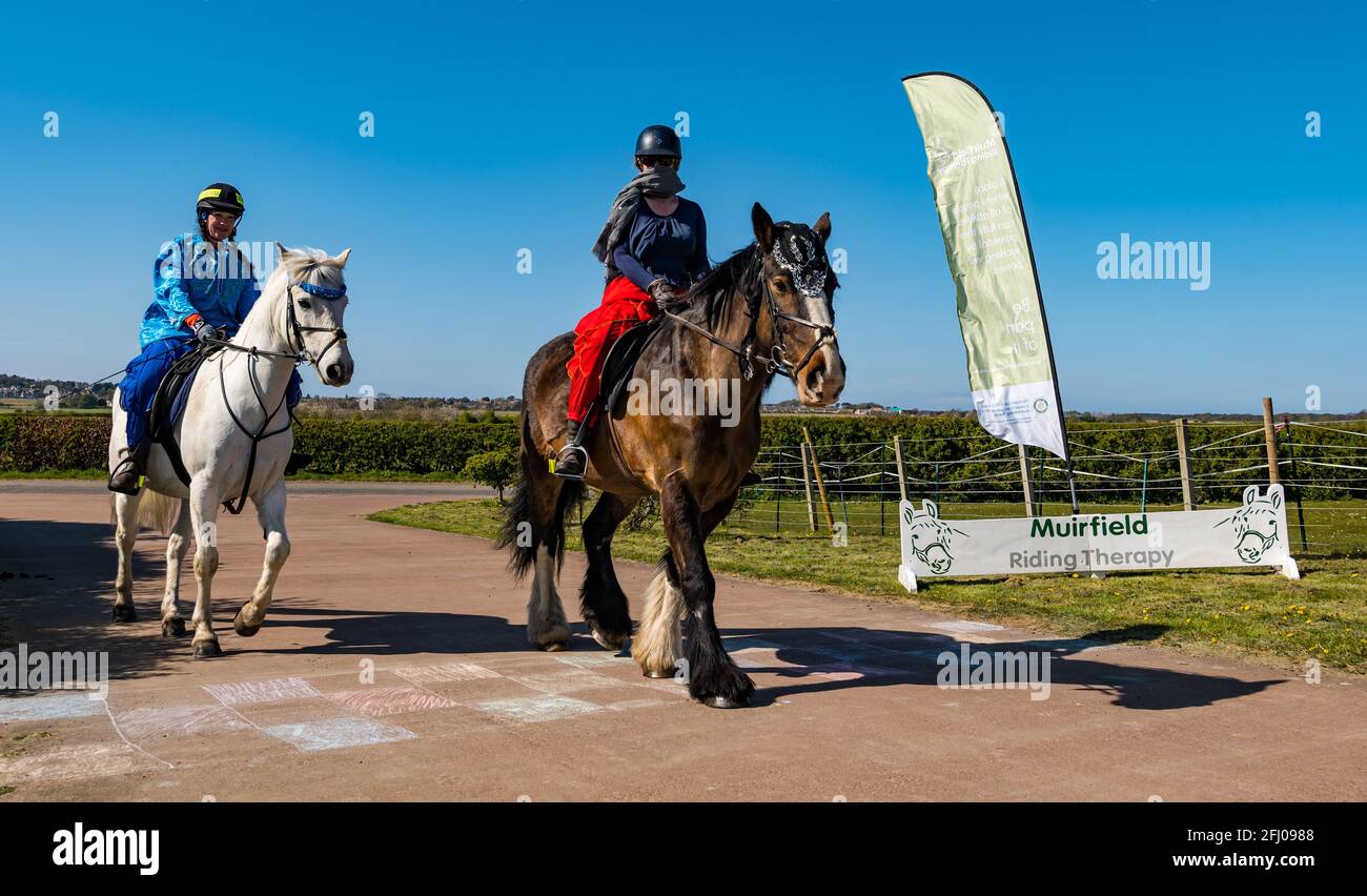 East Lothian, Schottland, Großbritannien, 25. April 2021. Virtueller Kilt Walk: Kilt Walker, die die Muirfield Riding Therapy Charity unterstützen, überqueren eine ‘Ziellinie’, um ihre Teilnahme an ihrer Spendenaktion ‘Round the World’ zu feiern. Im Bild: Morven McLelland auf Johnny & Charity, Therapiepferde unter Beccy O'Connor. Die Frauen und Pferde sind in arabischem Kostüm gekleidet, um die zurückgelegte Strecke darzustellen Stockfoto