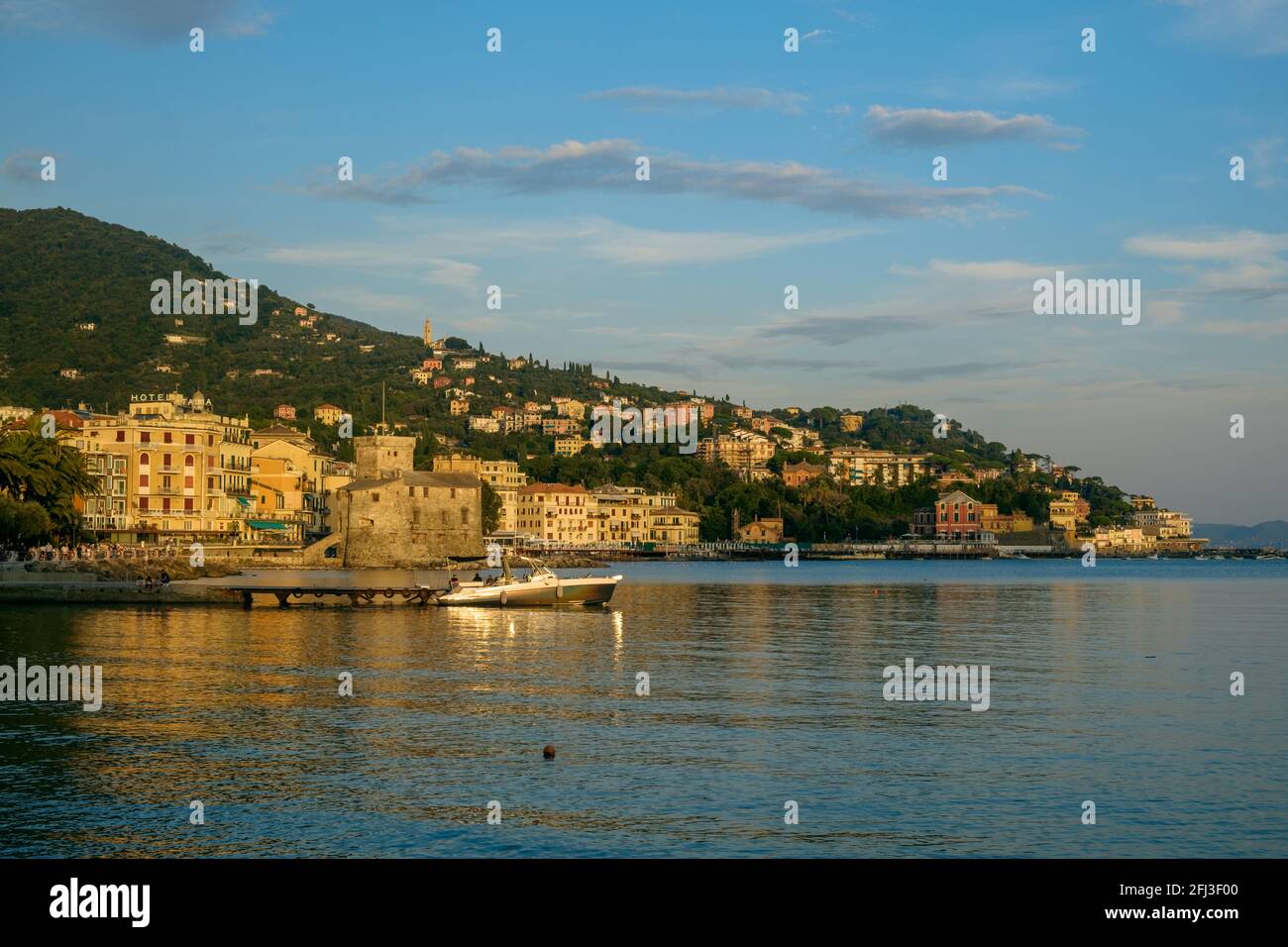 Ruhiges ligurisches Meer an der Küste von Rapallo. An Land und hinter der Burg werden auf einem bewaldeten Hügel Gebäude errichtet. Stockfoto