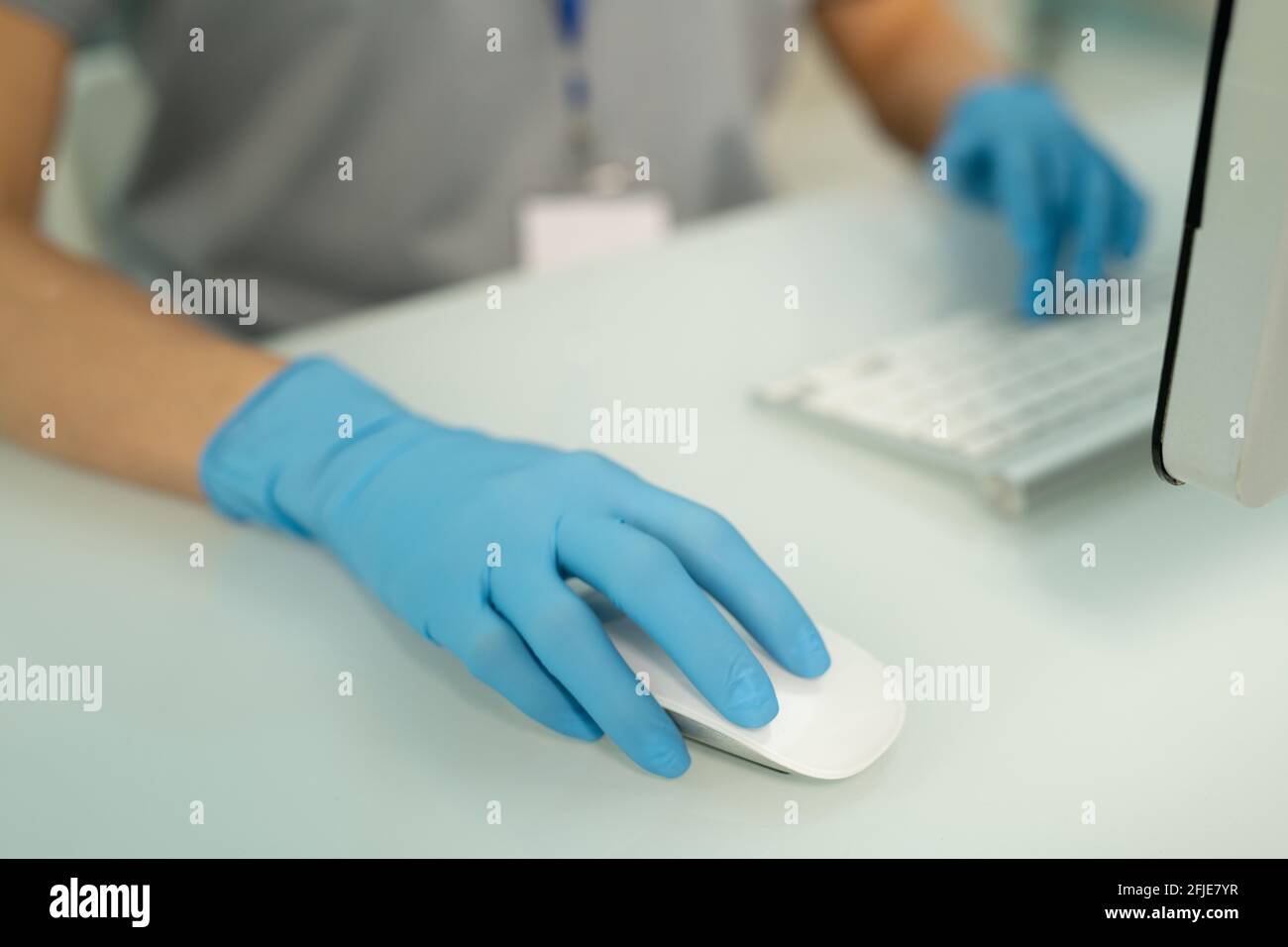 Nahaufnahme einer nicht erkennbaren Krankenschwester in blauen Handschuhen, die am Schreibtisch sitzen Und mit der Computermaus beim Ausfüllen von Online-Patientenakten Stockfoto