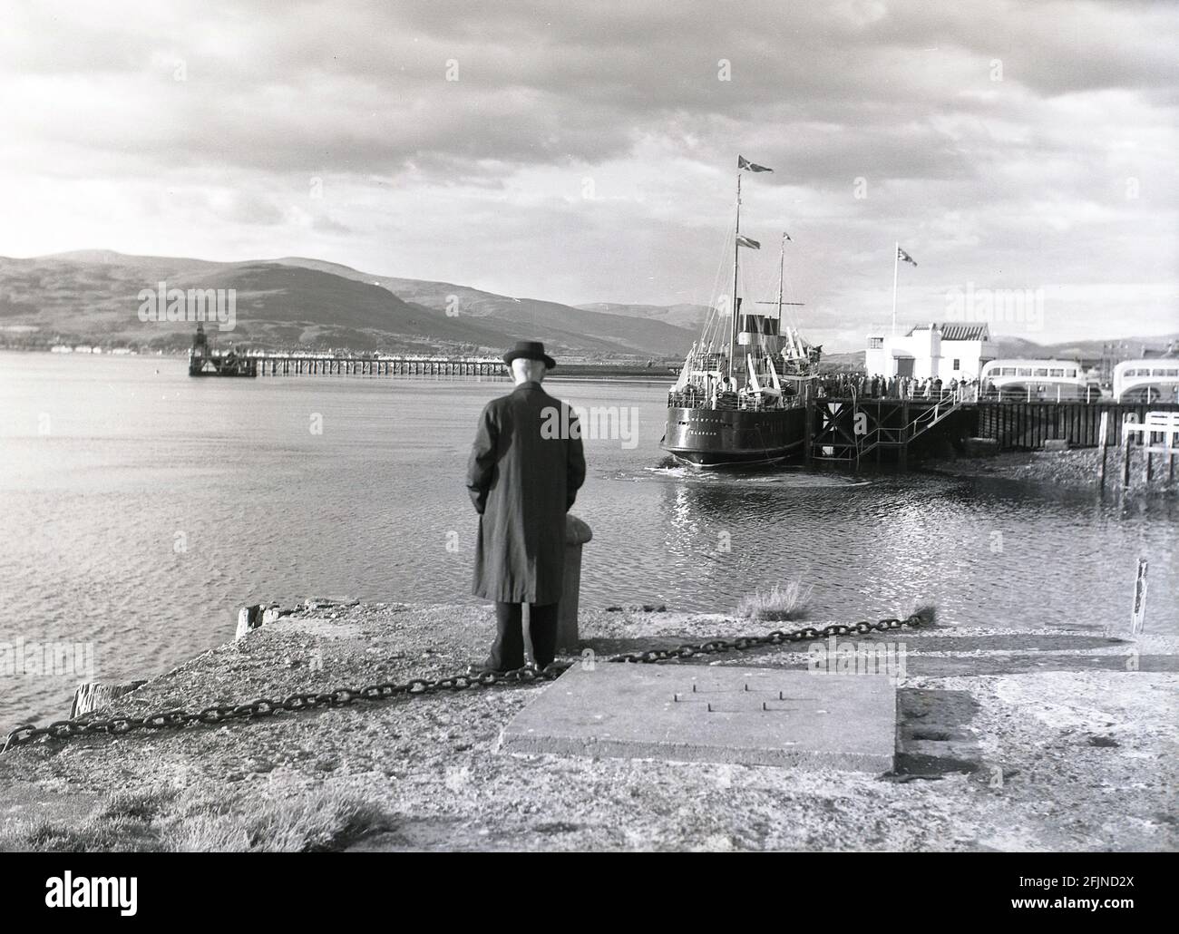 1956, historisch, ein Mann, der am Kai neben einem loch auf den Western Isles steht und Passagiere beim Einsteigen in den Postdampfer beobachtet, Lochfyne of Glasgow, Scottish Highlands, Schottland, Großbritannien. Die von William Denny und Brothers gebaute MV Lochfyne war ein MacBrayne-Postdampfer, der 1931 für den West Highland Service, das erste britische Küstenpassagierschiff mit Diesel-elektrischem Antrieb, gebaut wurde. 1958 wurde sie das ganze Jahr über das Boot Ardrishaig. 1969 wurde sie aus dem Dienst zurückgezogen. Stockfoto